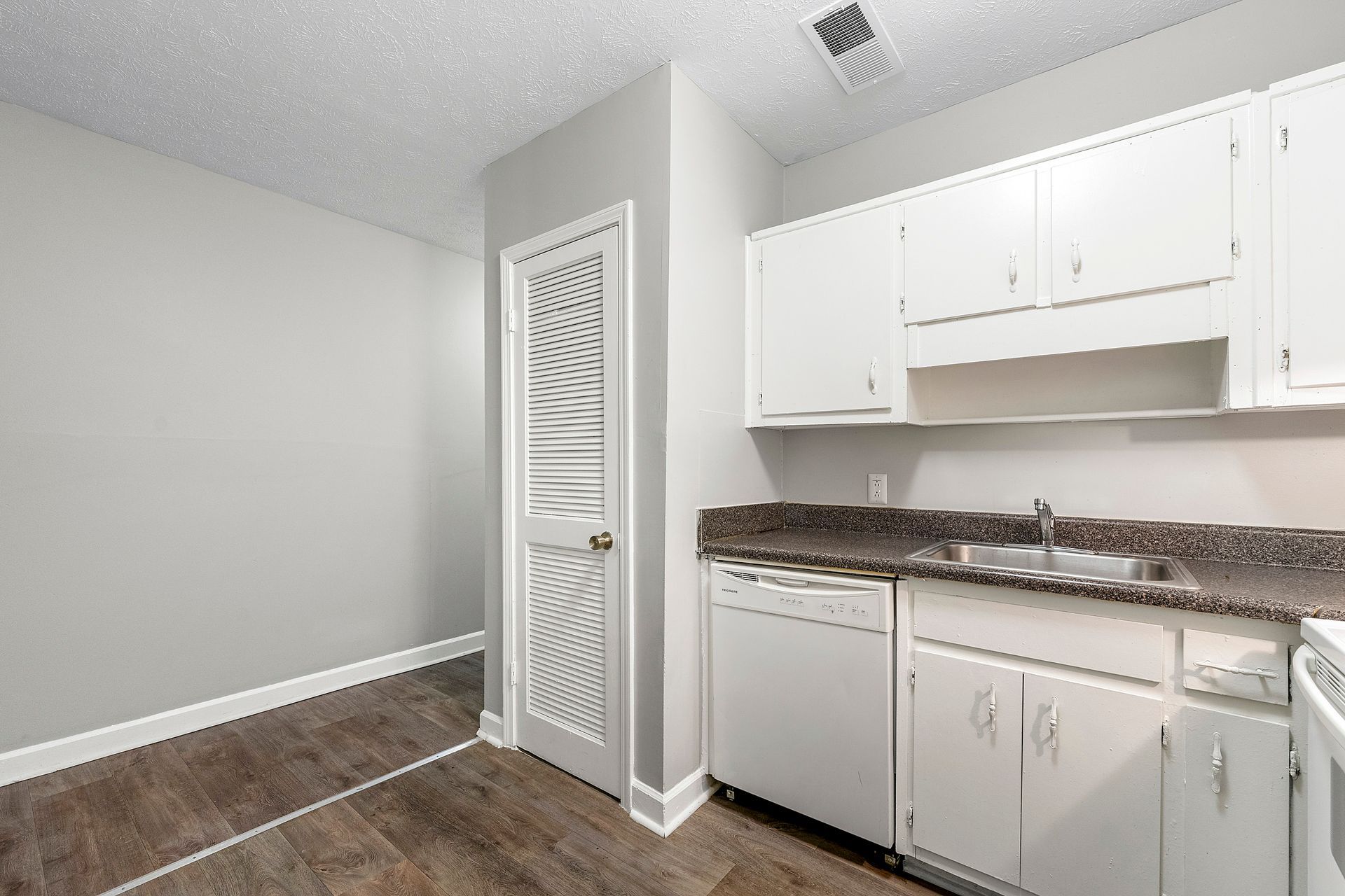Small kitchen with white cabinets, granite countertop, sink, and a decorative pantry door on wood flooring.