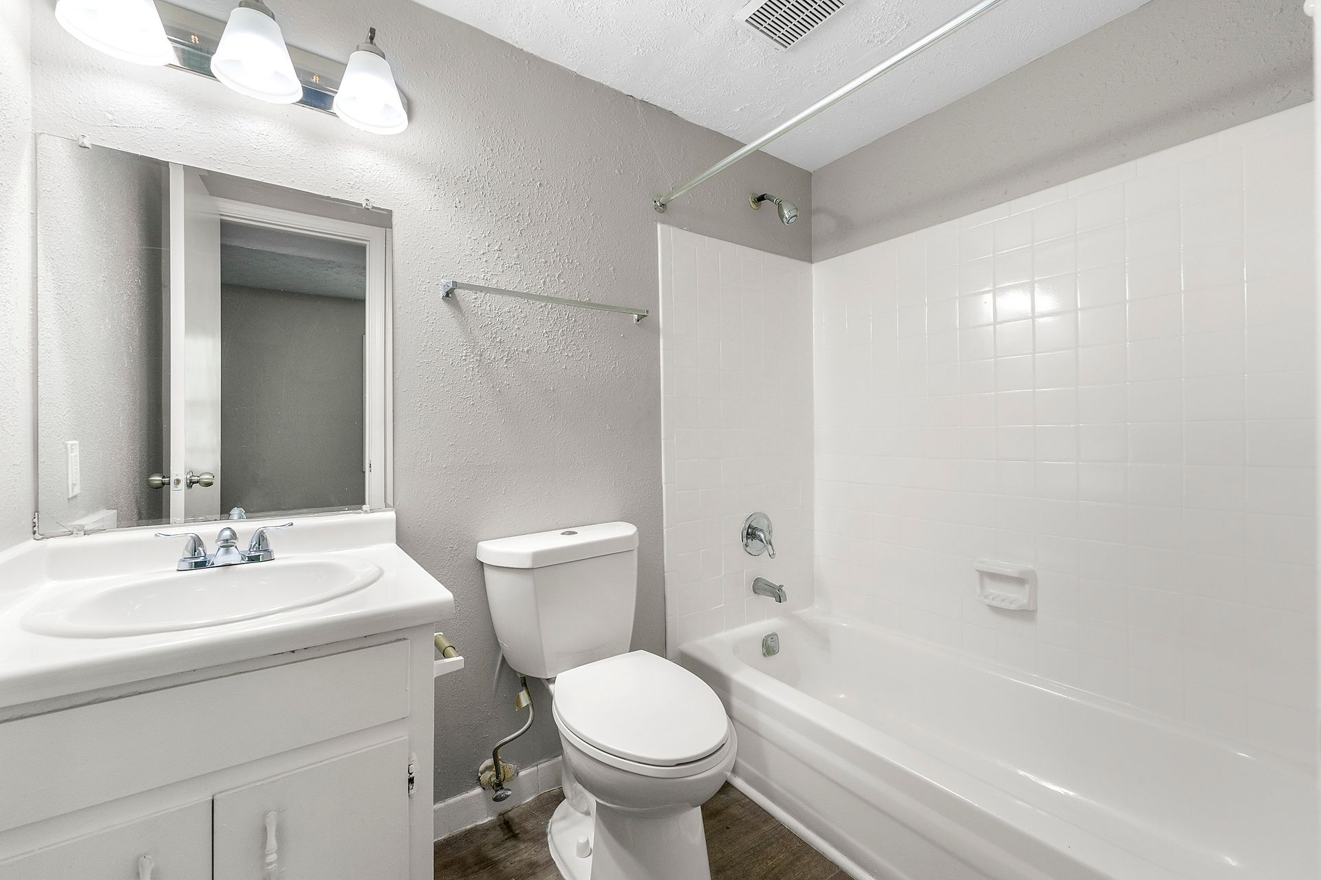 Small white bathroom with vanity, toilet, bathtub, and bright overhead lights.