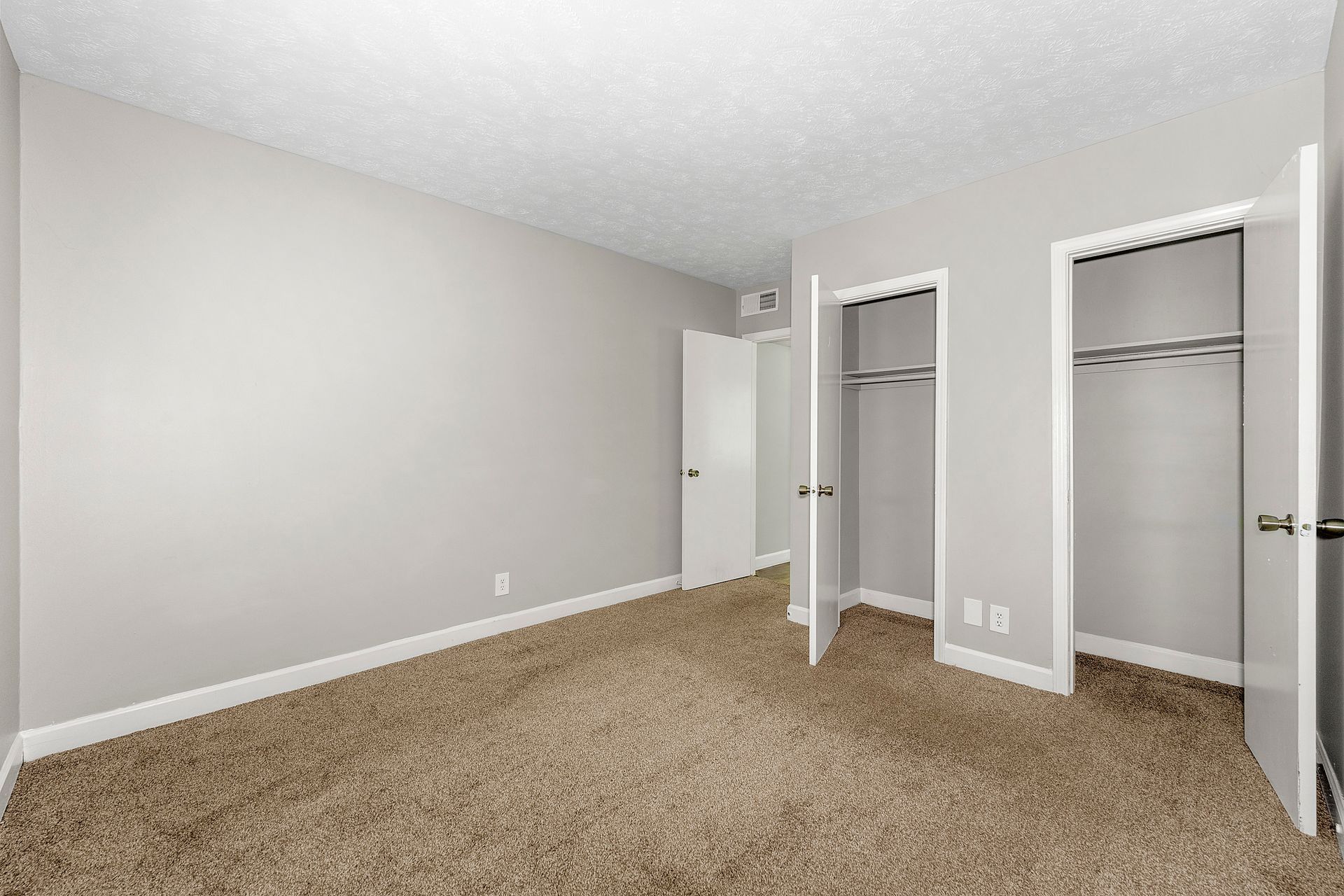 Empty beige bedroom with carpeted floor and open closet doors