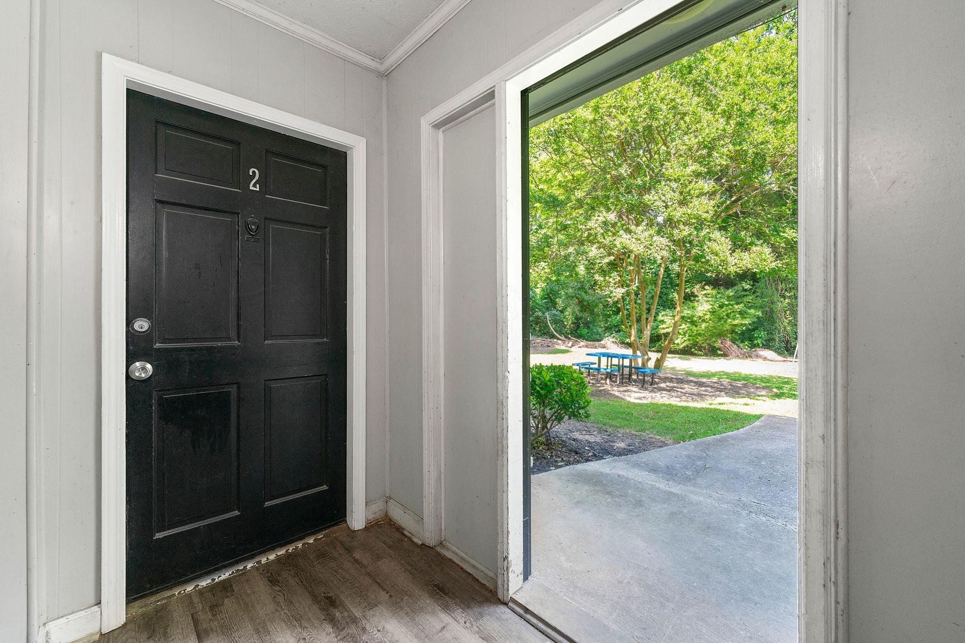 Front entryway with a black door and an open doorway showing a tree-lined sidewalk outside