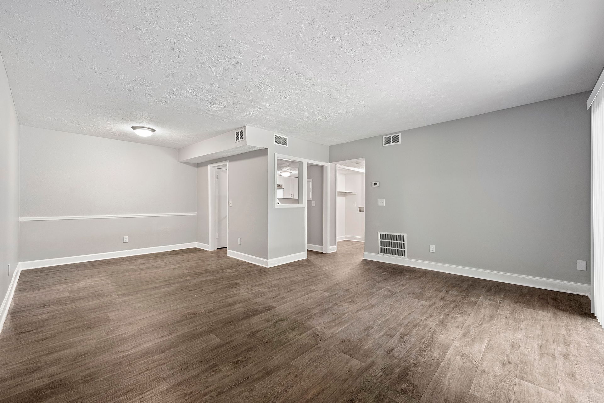 Empty carpeted living room with gray walls and white trim, view toward a doorway and ceiling fan