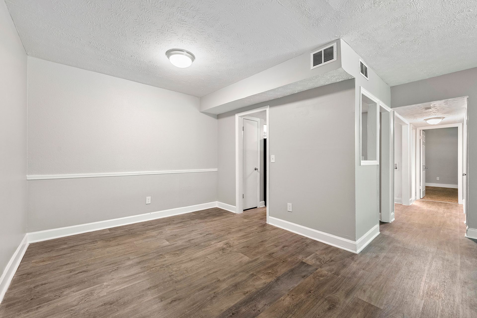 Empty gray room with wood-look flooring, white trim, and an open hallway