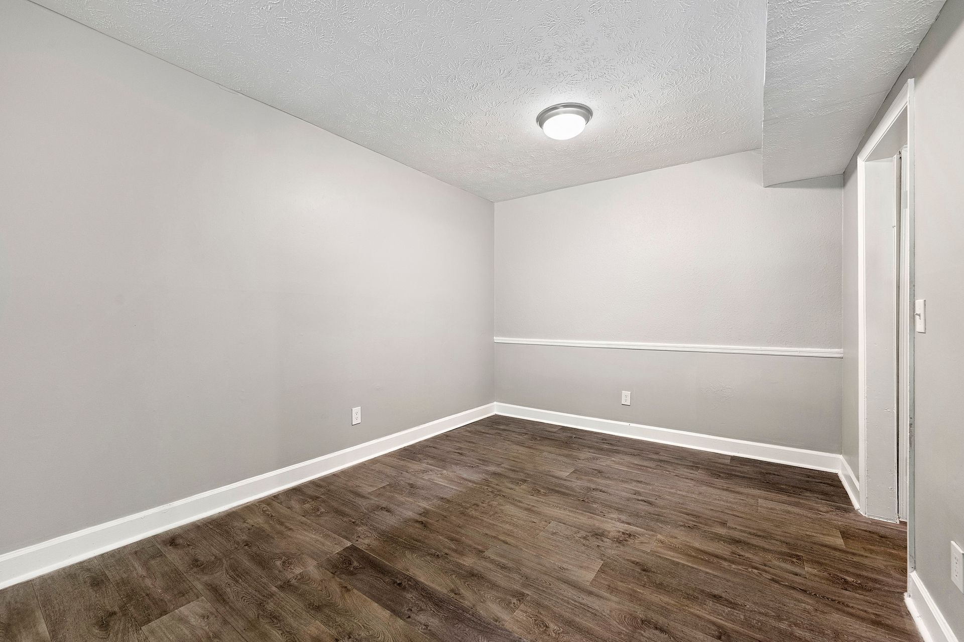 Empty gray bedroom with wood-look flooring and white trim, lit by a ceiling light.