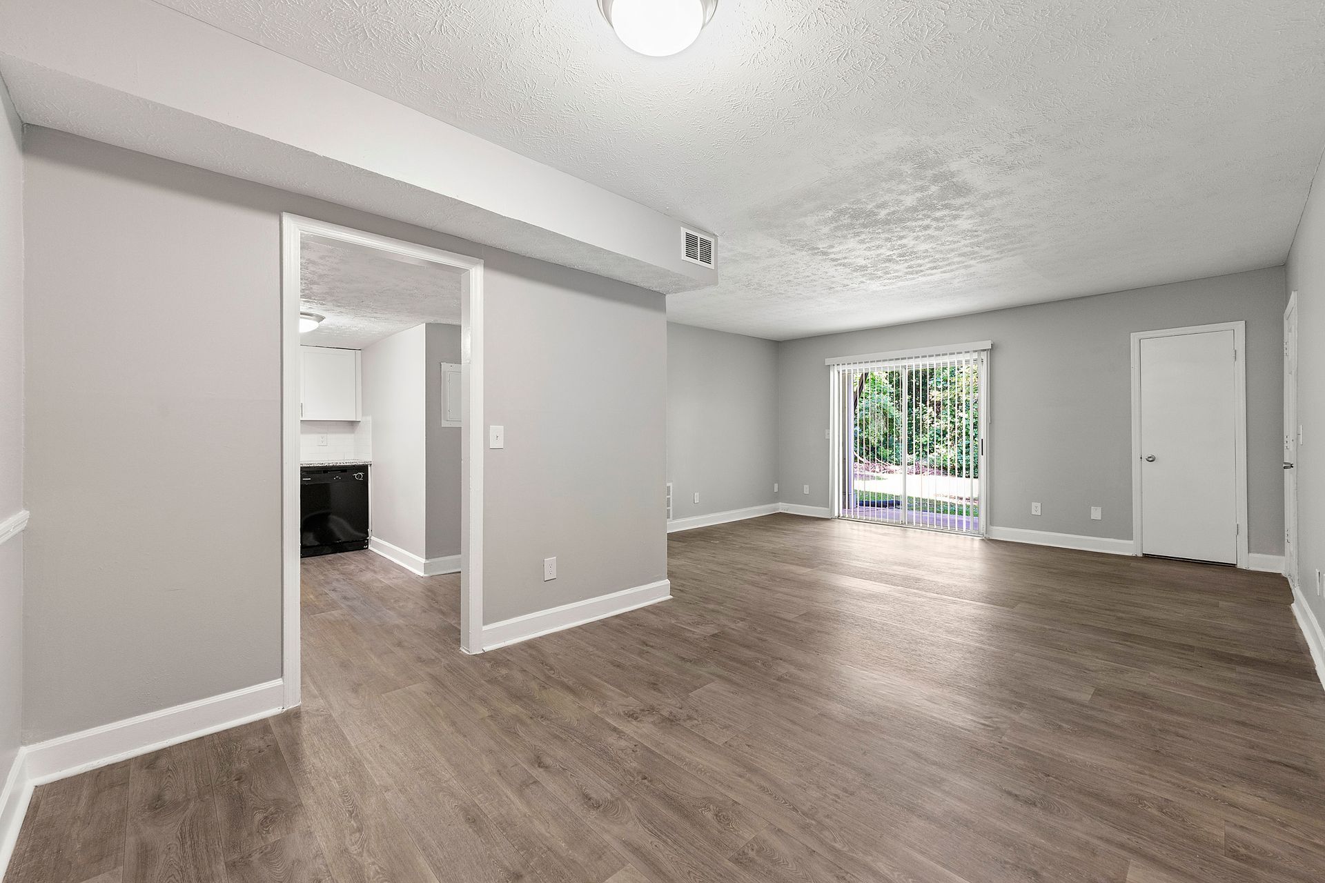 Empty gray living room with wood floors and sliding glass doors to a balcony