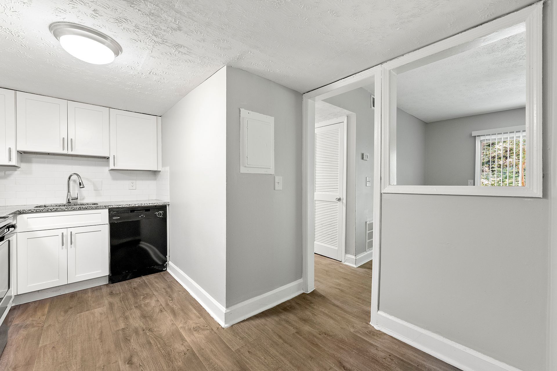 Small open apartment with white kitchen, black stove, wood floors, and pass-through to hall and windowed room