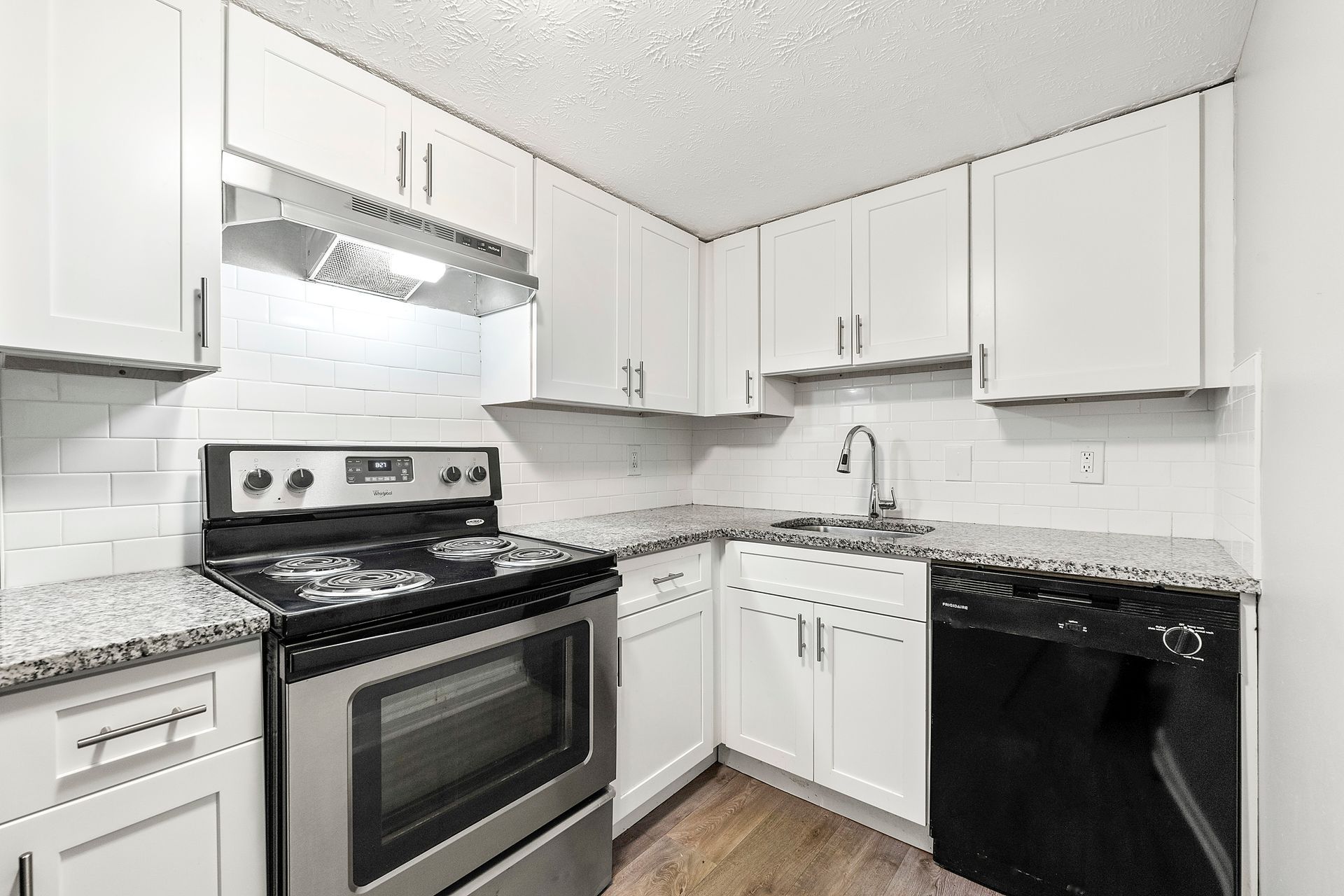 Bright white kitchen with stainless steel stove, black dishwasher, and granite countertops.
