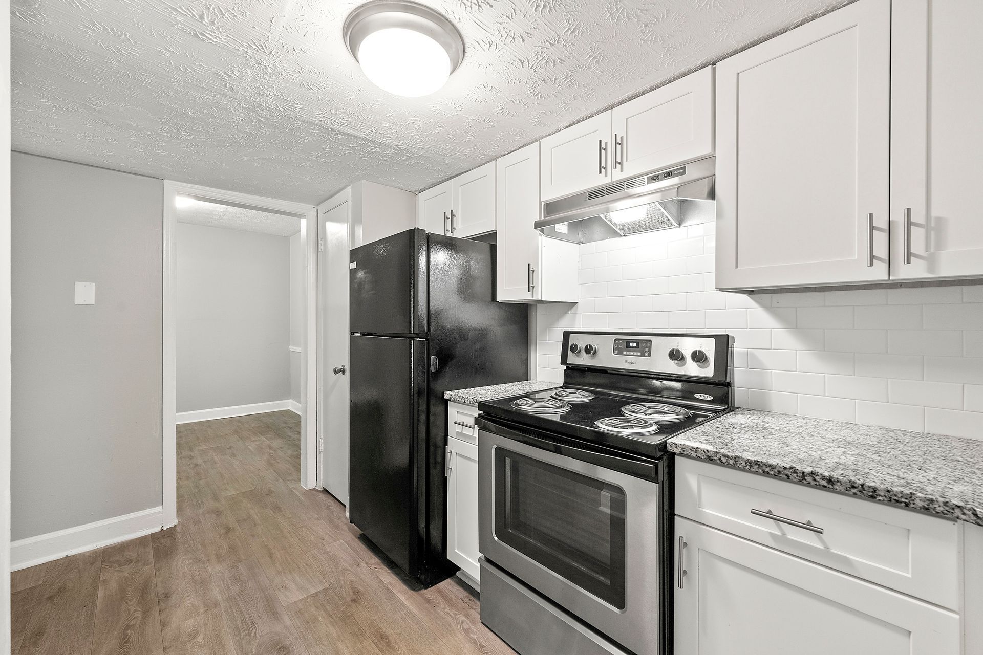 Modern kitchen with black appliances, white cabinets, granite countertops, and light wood flooring.