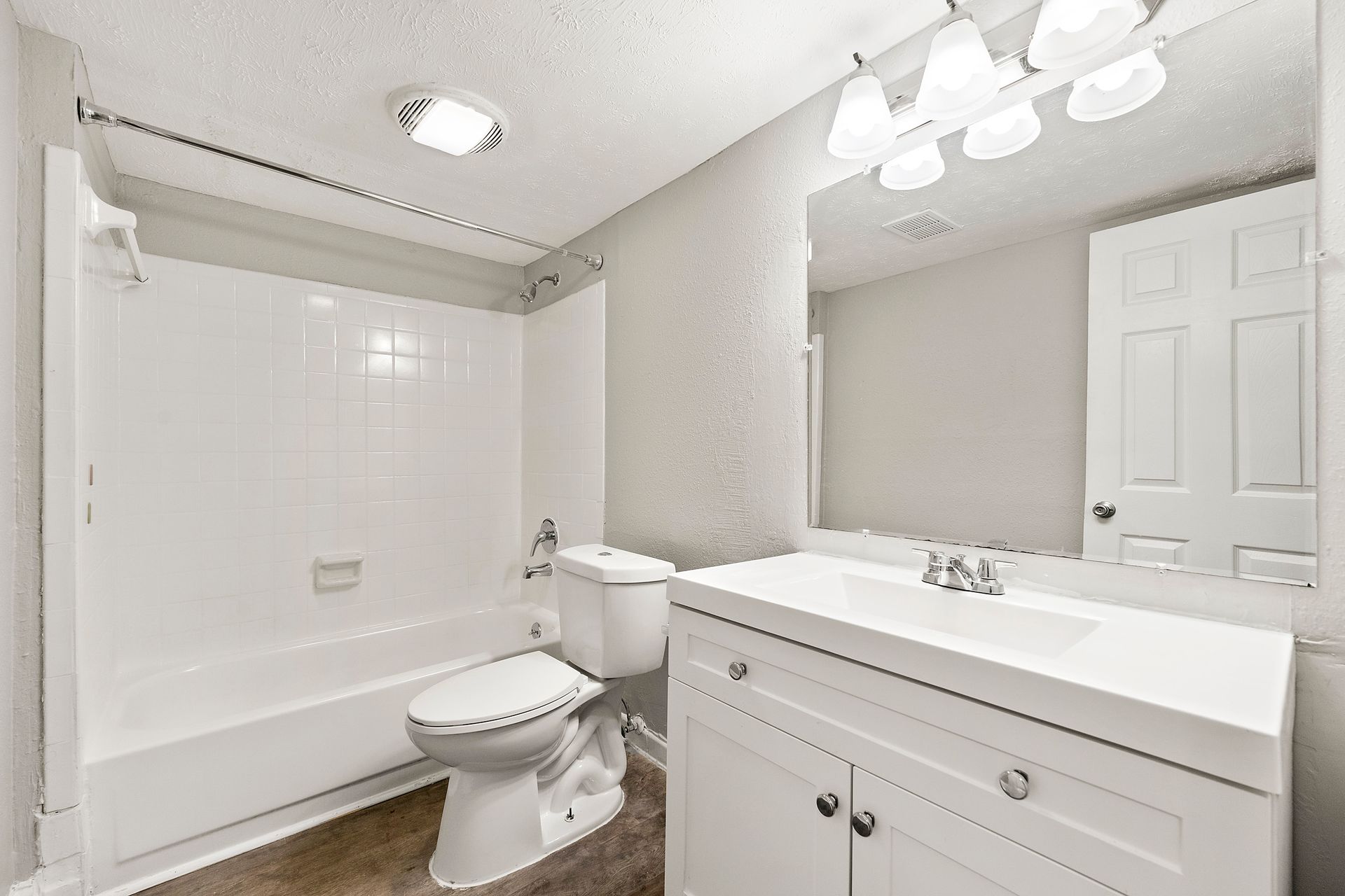 Bright white bathroom with bathtub, toilet, vanity sink, and overhead lights