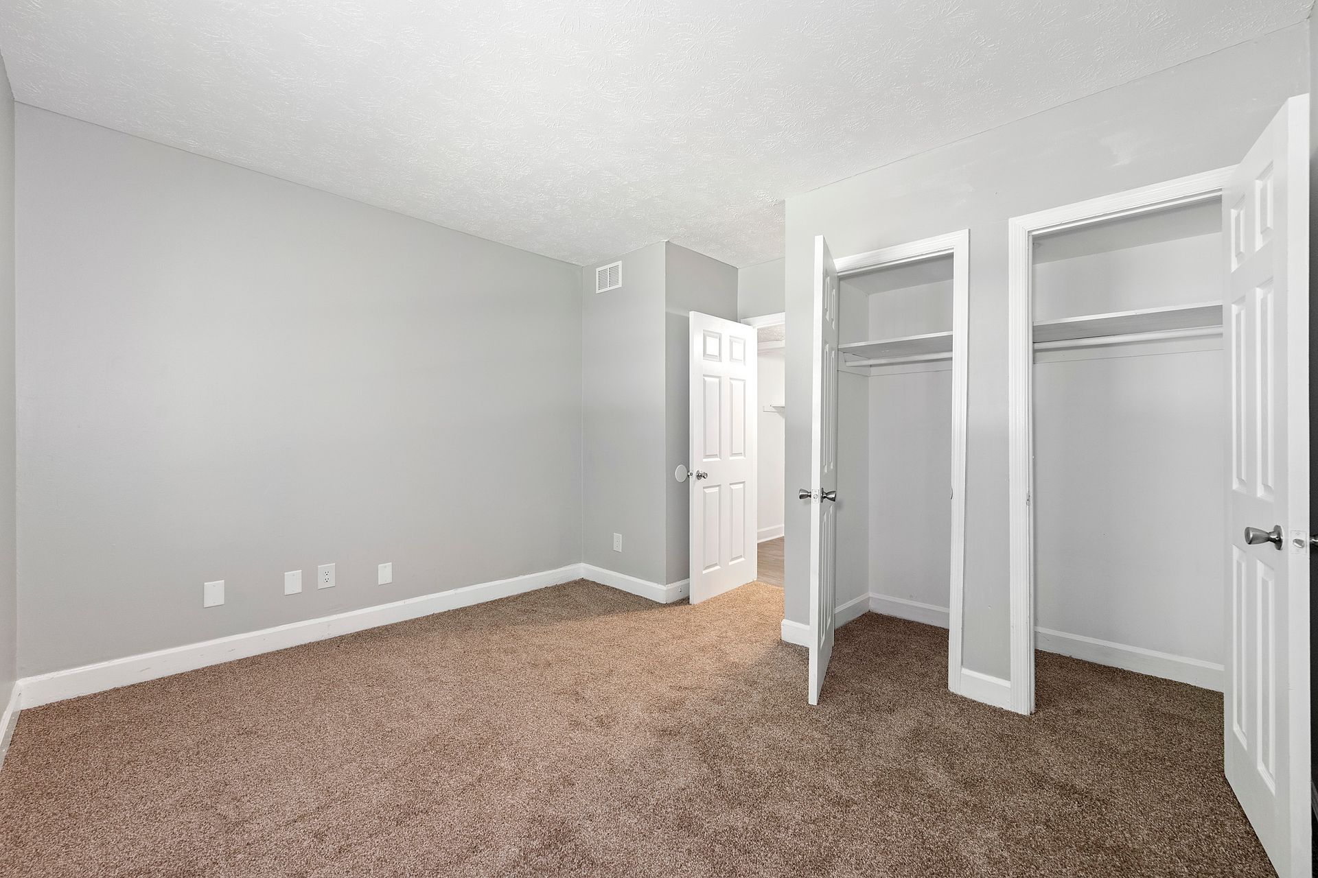Empty beige bedroom with gray walls, carpeted floor, and open closet doors.