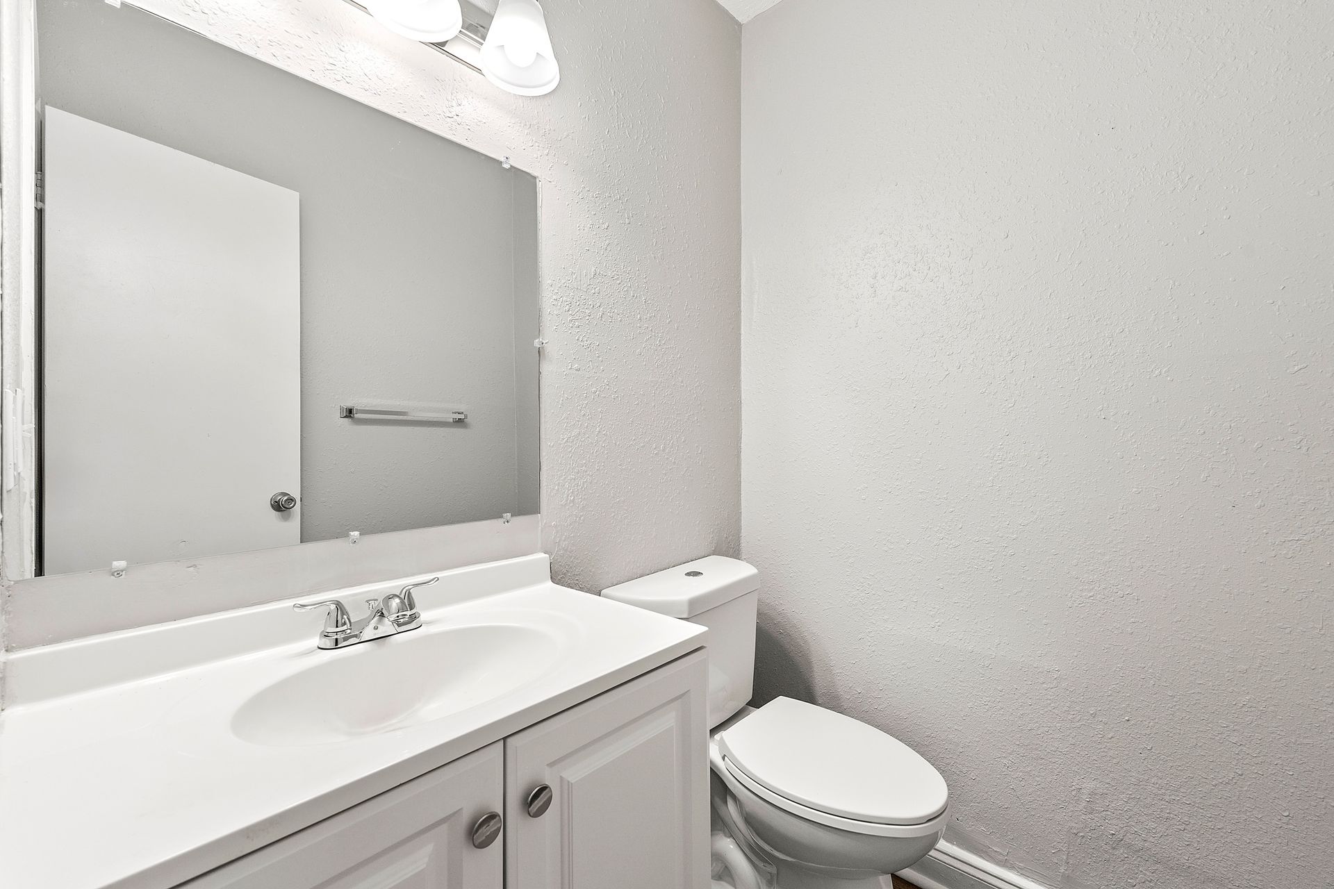 Bright white bathroom with vanity sink, mirror, and toilet against textured walls.