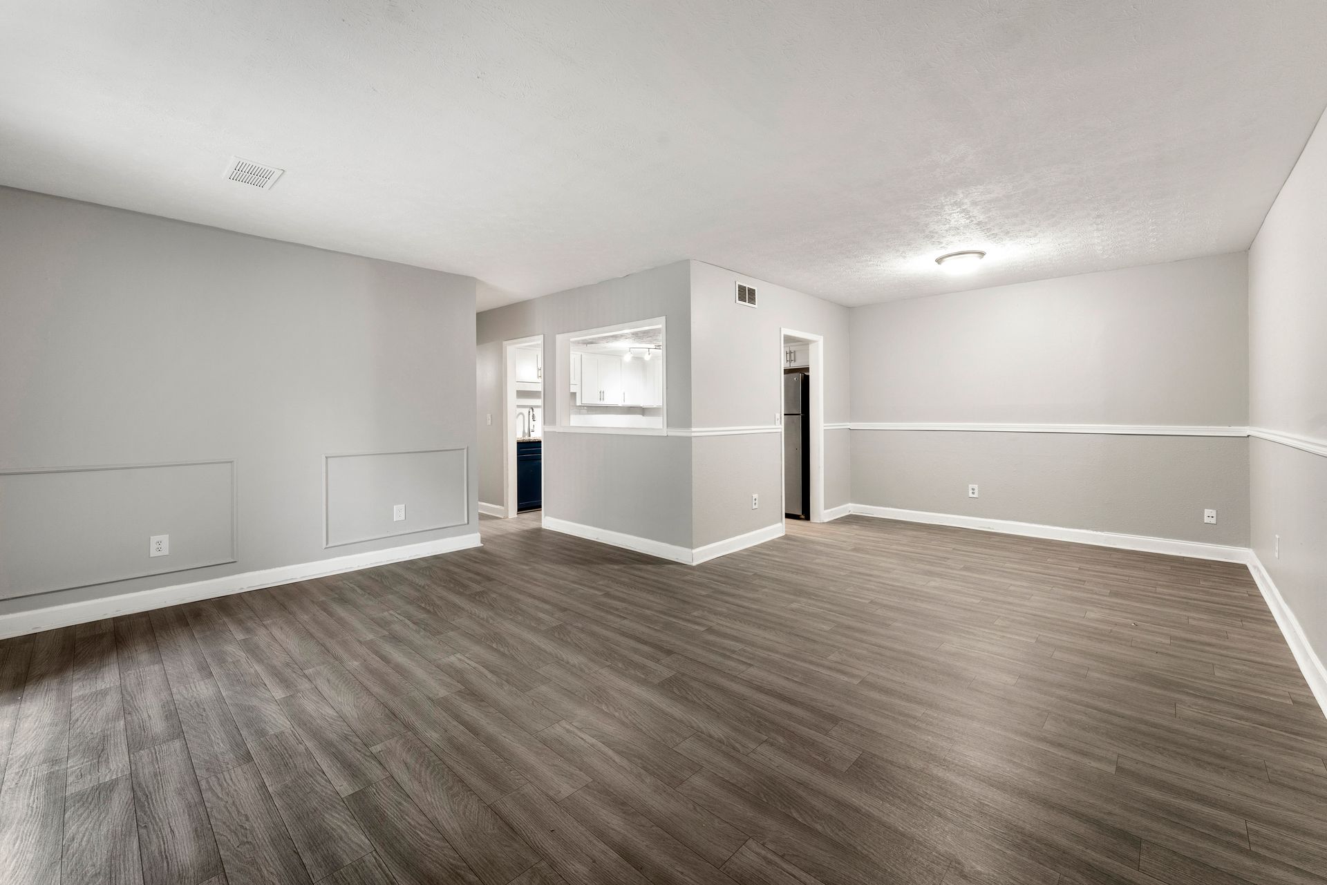 Empty open-plan living room with gray walls, white trim, and wood-look flooring