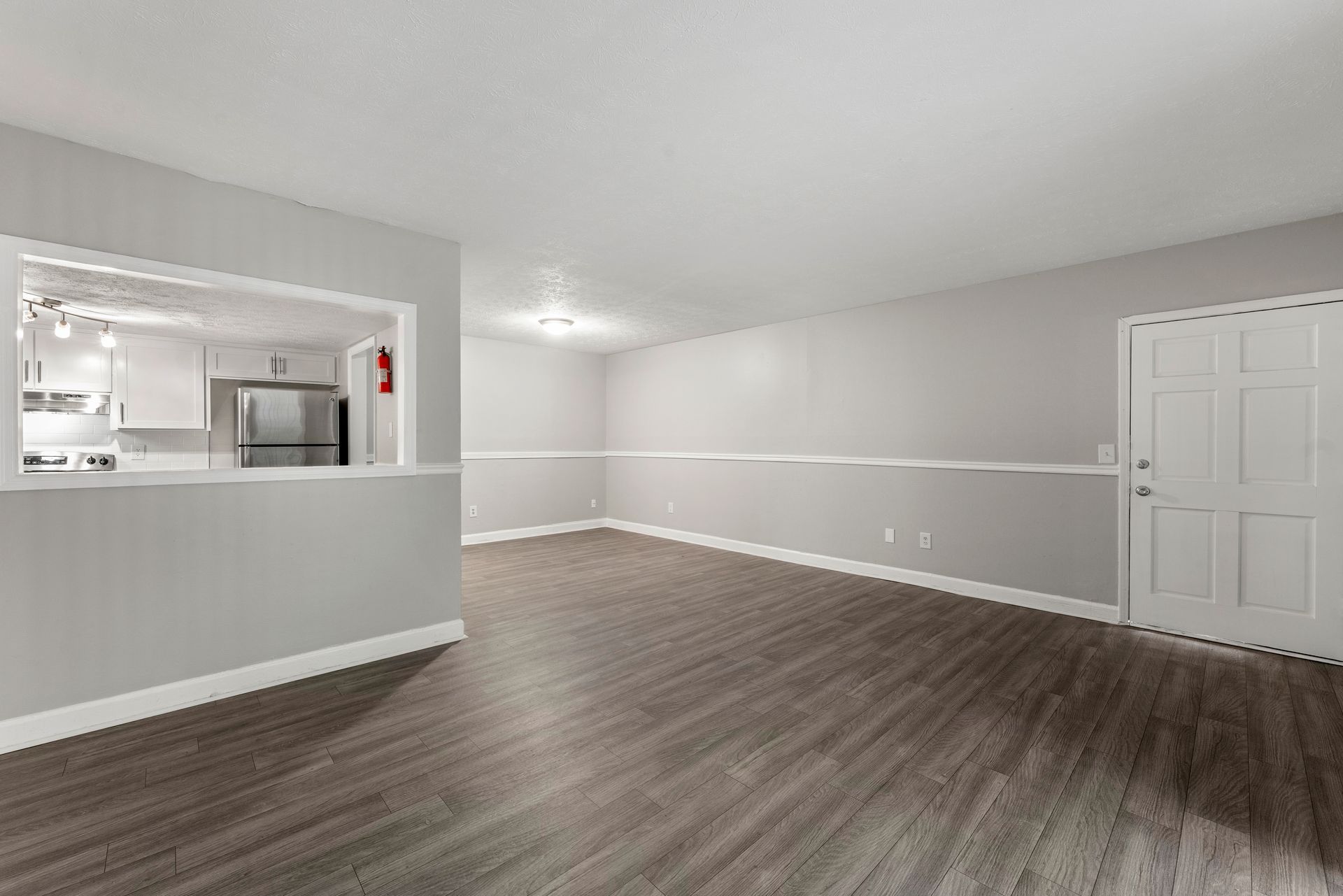Empty living room with gray walls, dark wood flooring, and an open pass-through to the kitchen.