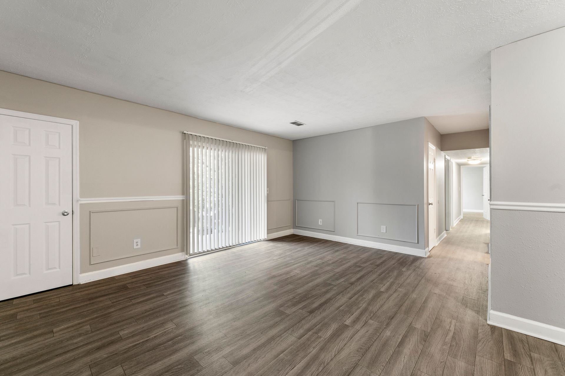 Empty beige living room with gray wood floors, white trim, and sliding glass doors.