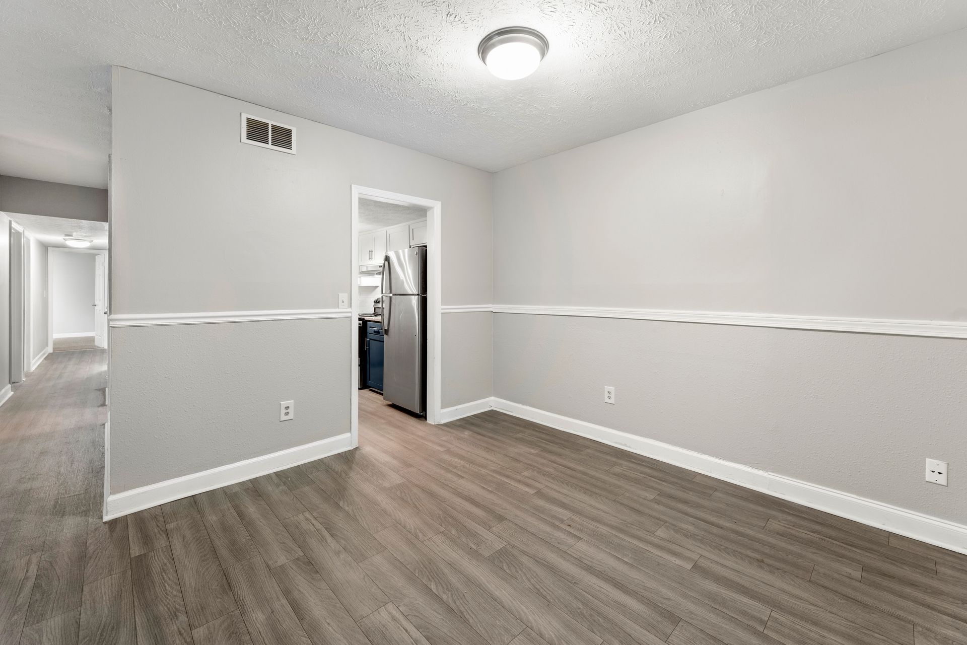 Empty gray room with wood-look floors, white trim, and an open doorway to a bathroom.