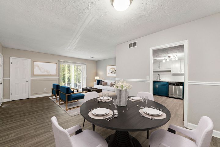 Open-plan dining and living room with dark table, blue chairs, gray carpet, and white walls.