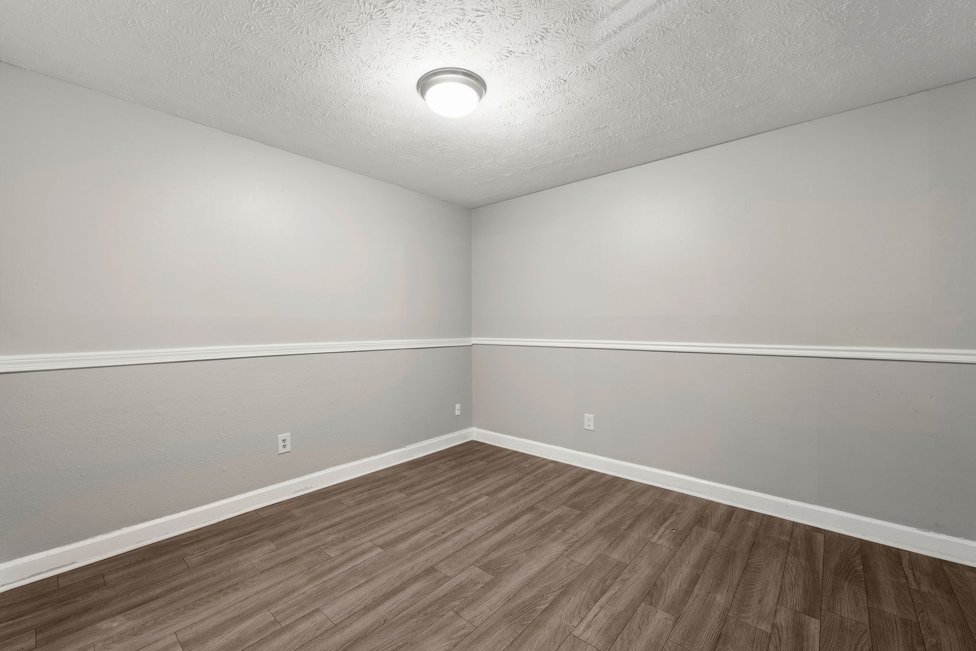 Empty gray room with wood-look flooring, white trim, and a ceiling light.