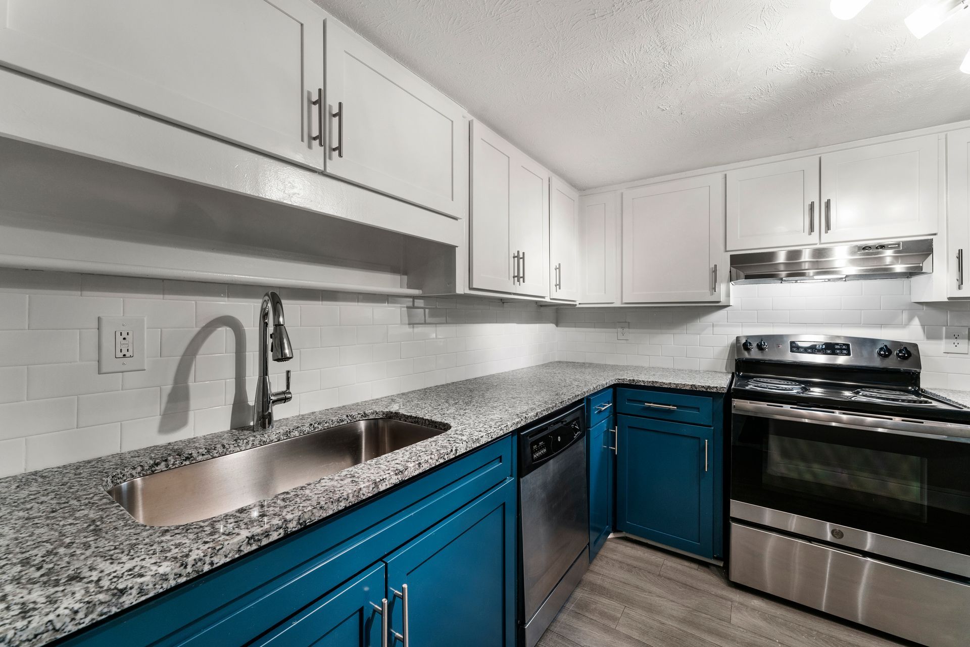 Modern kitchen with white cabinets, granite counters, blue lower cabinets, and stainless steel appliances
