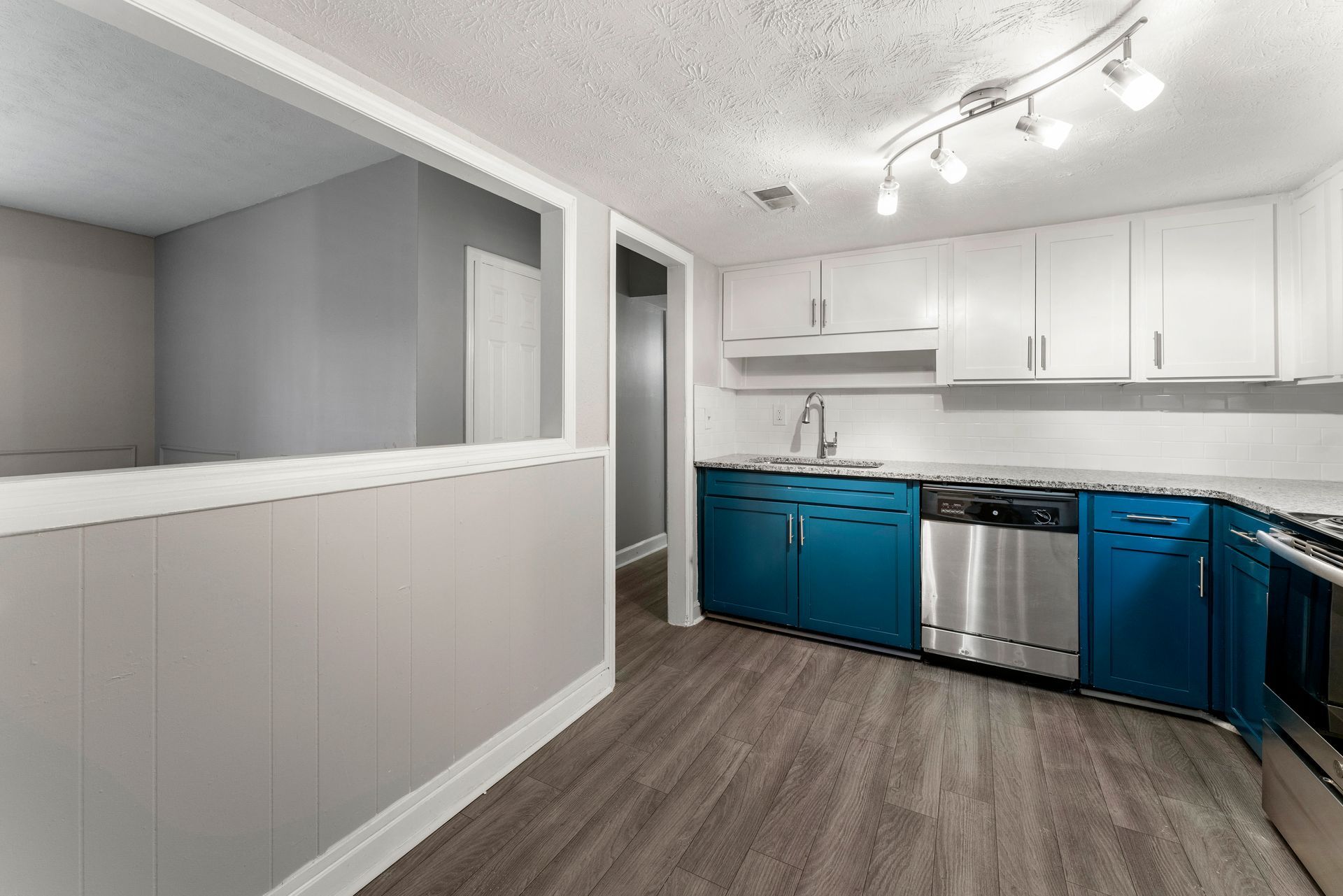 Empty kitchen with white cabinets, blue lower cabinets, stainless stove, and gray wood flooring