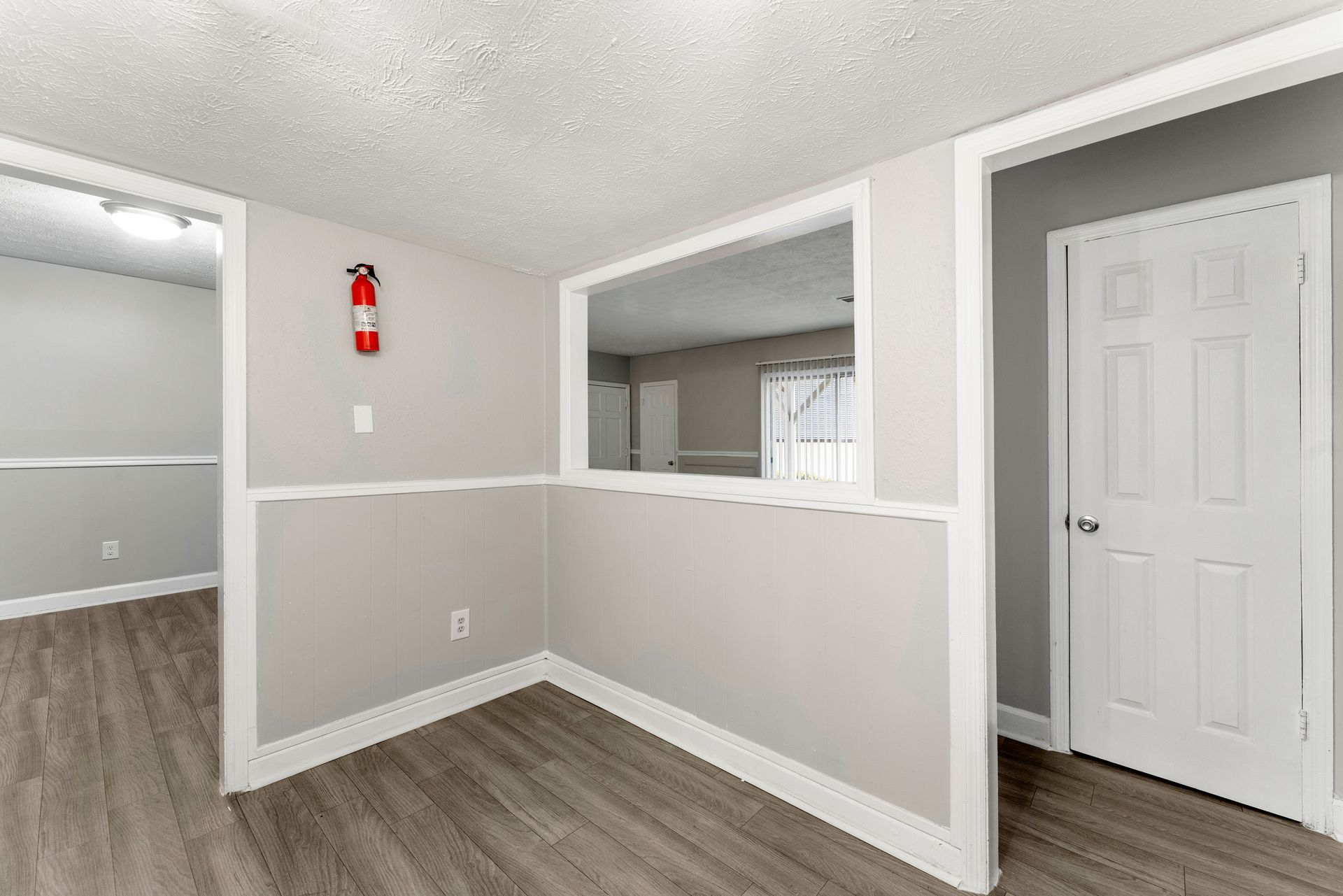 Empty gray interior with white trim, wood floors, open doorway, and a red fire extinguisher on the wall