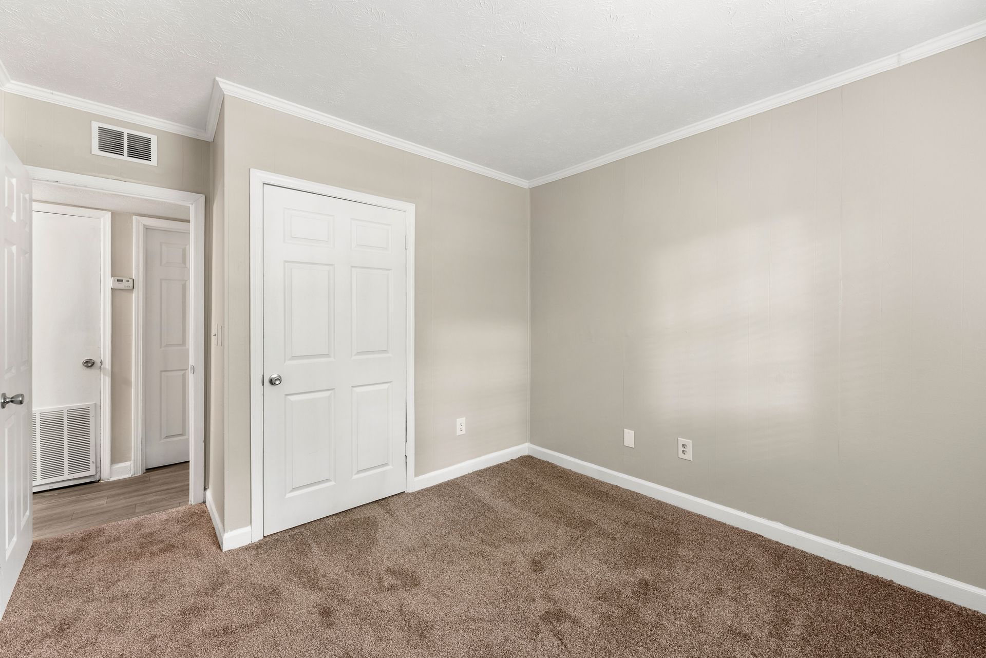 Empty beige bedroom with carpet, white doors, and a closet.