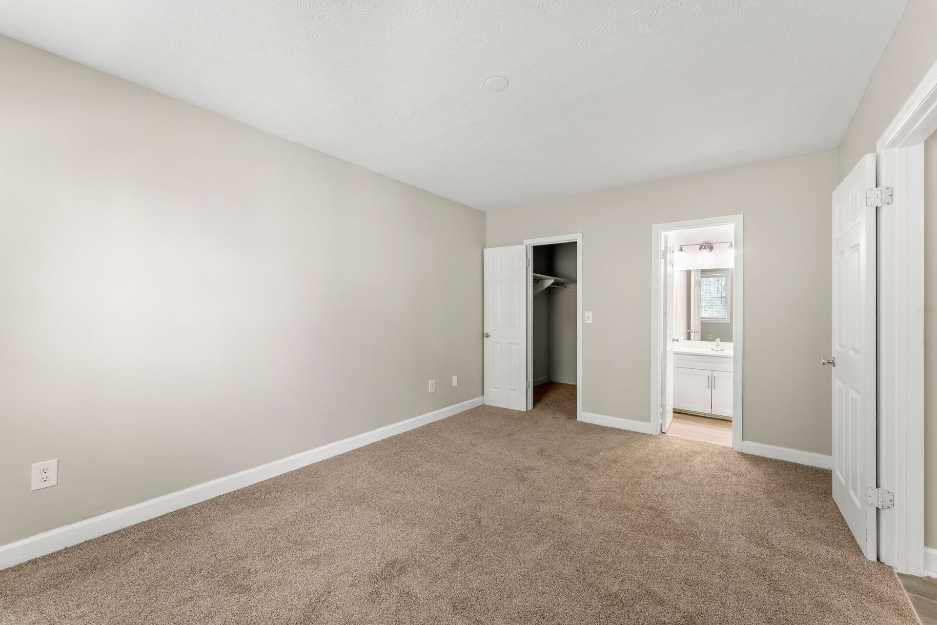 Empty beige bedroom with carpet, open closet, and doorway to a bathroom