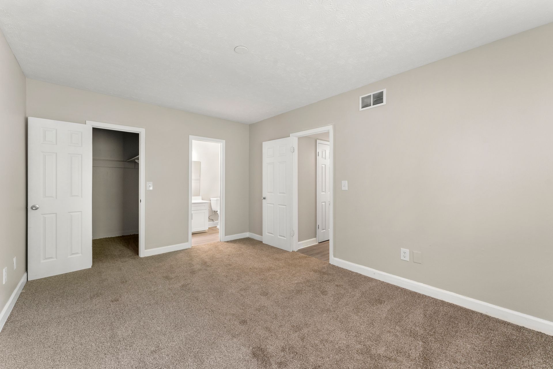 Empty beige bedroom with carpet, white doors, and an open closet area