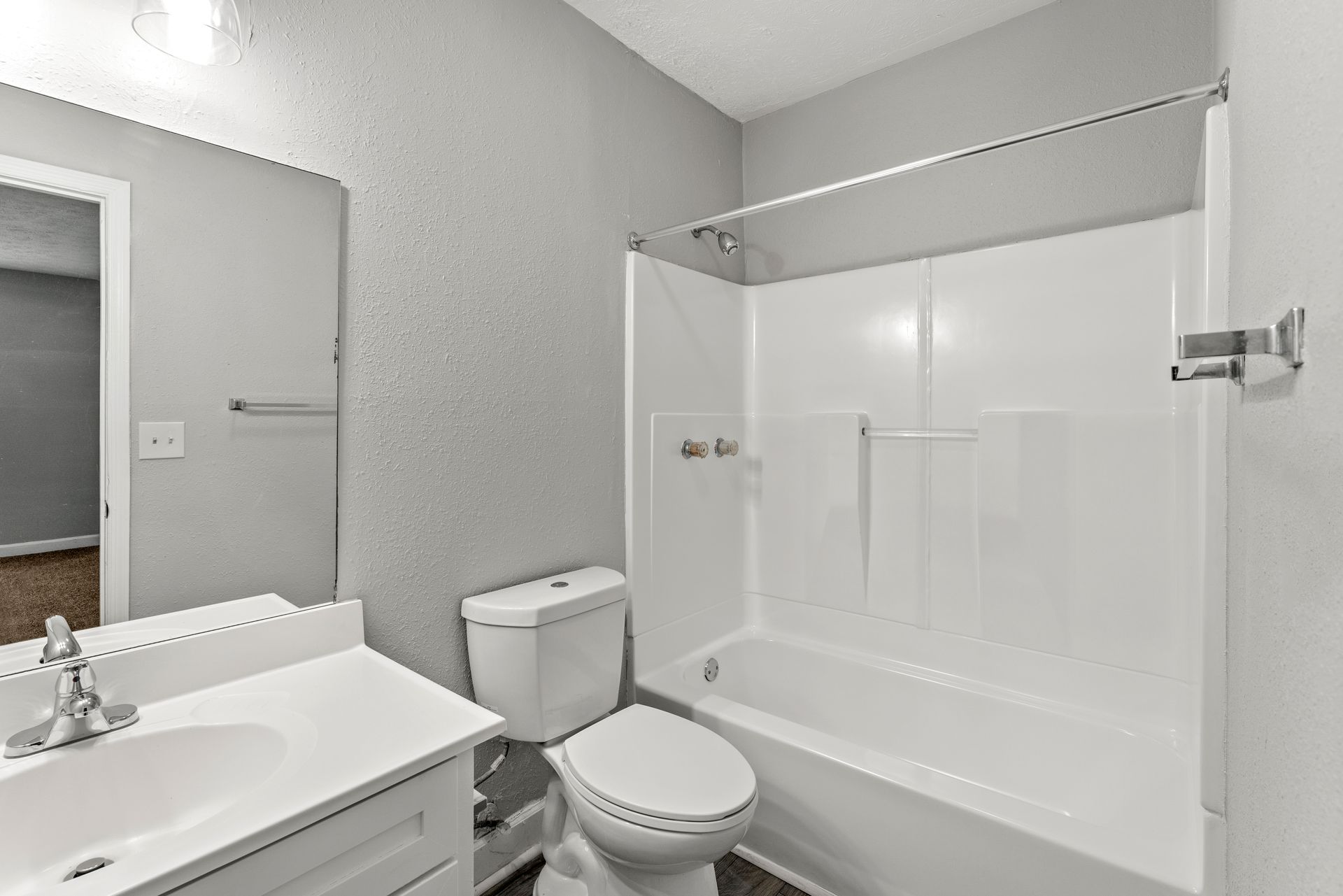 Bright bathroom with white vanity, toilet, and tub-shower combo against gray walls.