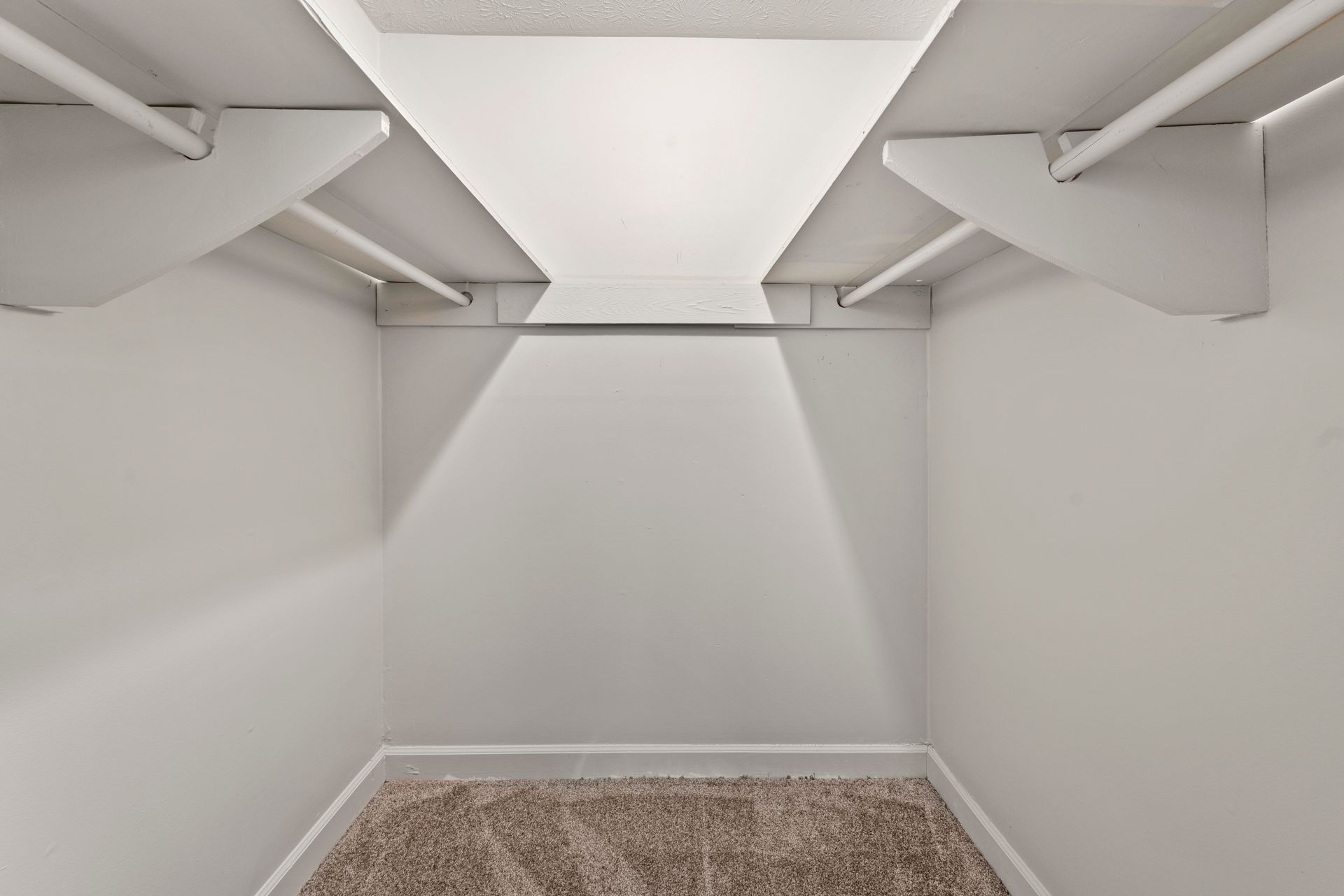 Empty walk-in closet with white walls, shelves, and carpeted floor with wire hanging rods.