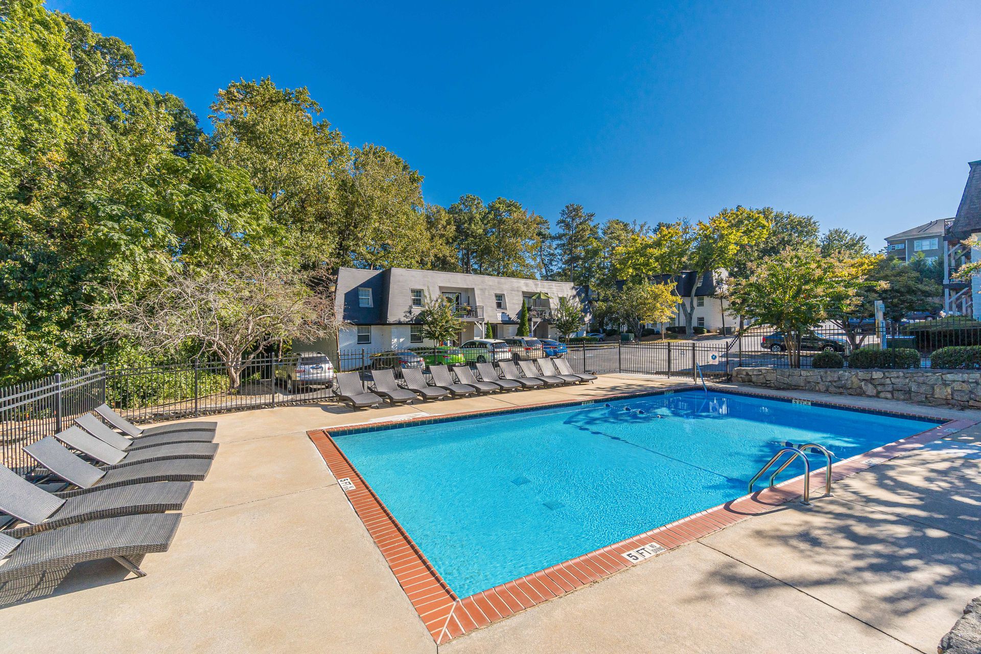 Outdoor swimming pool with blue water, lounge chairs, and trees under a clear sky