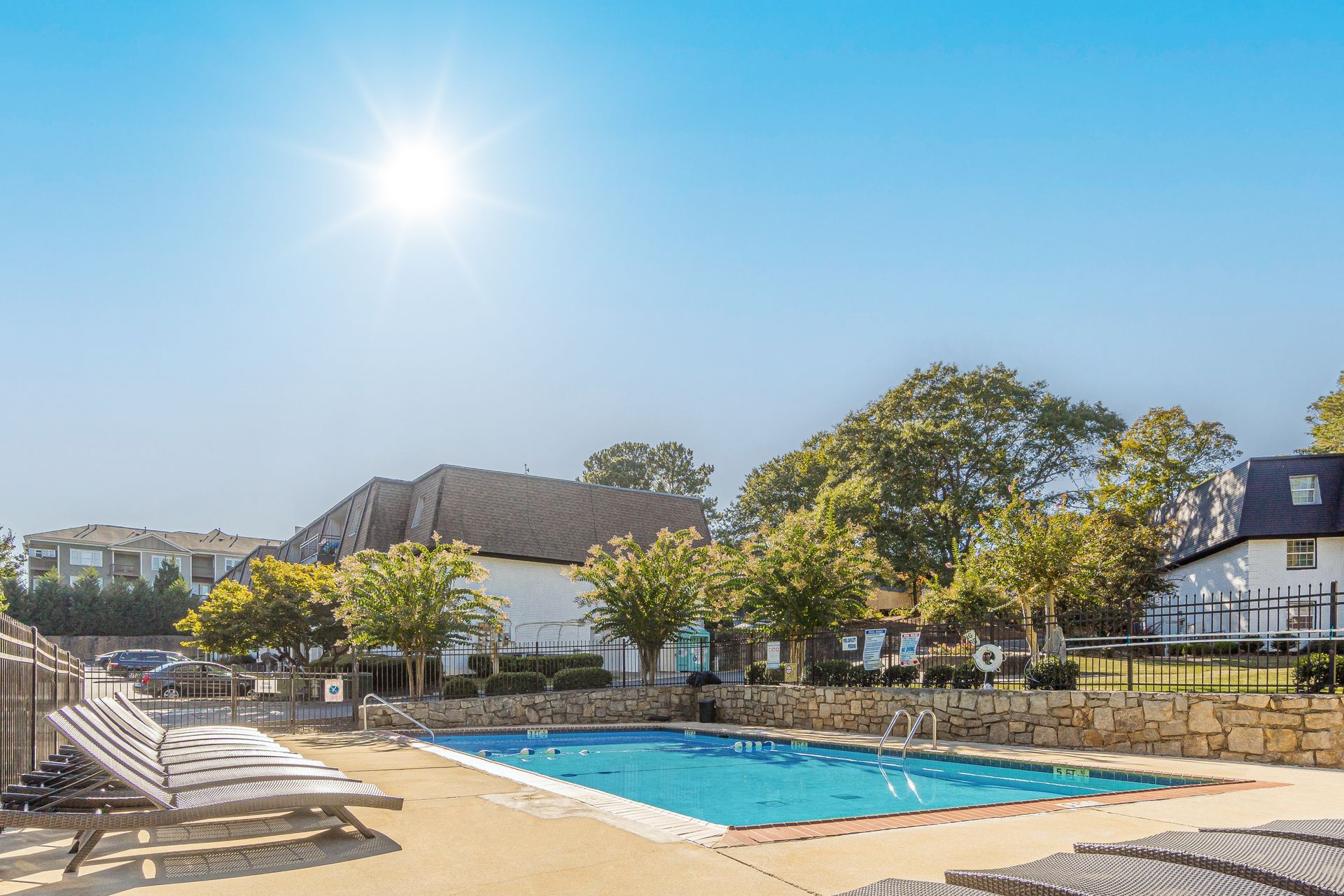 Sunny outdoor pool with lounge chairs and trees beside houses