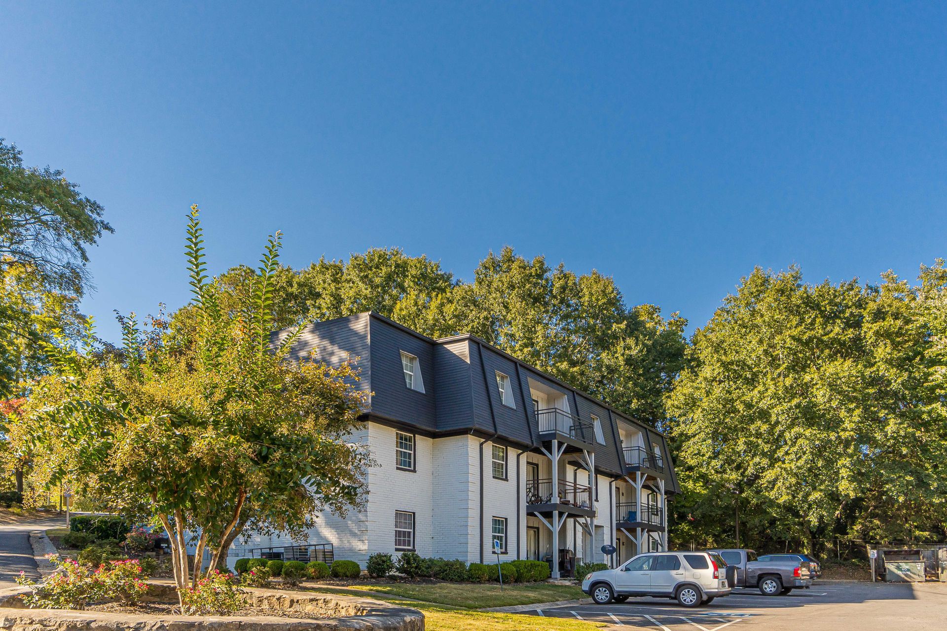 Apartment building with parked cars and trees under a clear blue sky