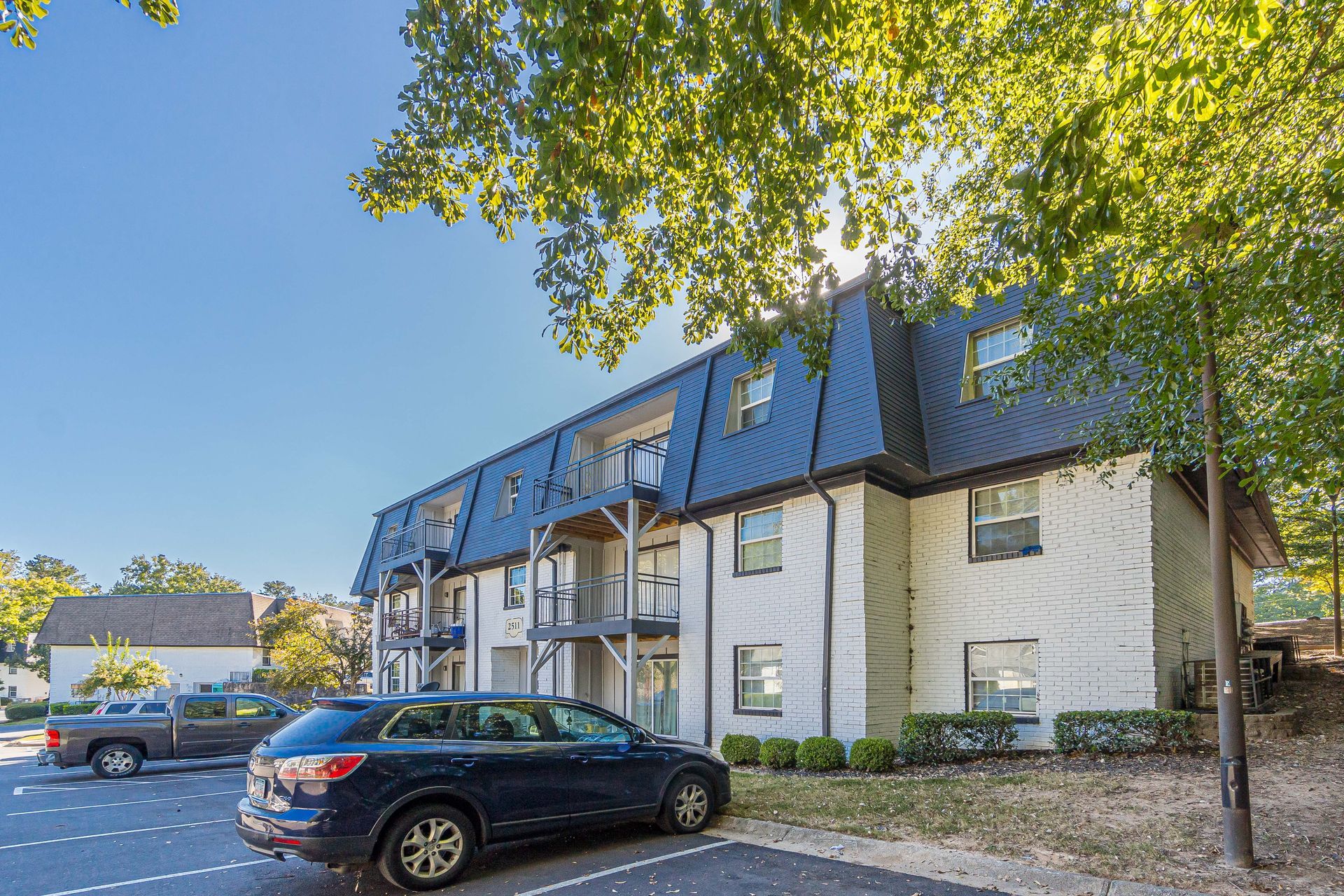 Apartment building with parked cars under leafy trees on a sunny day