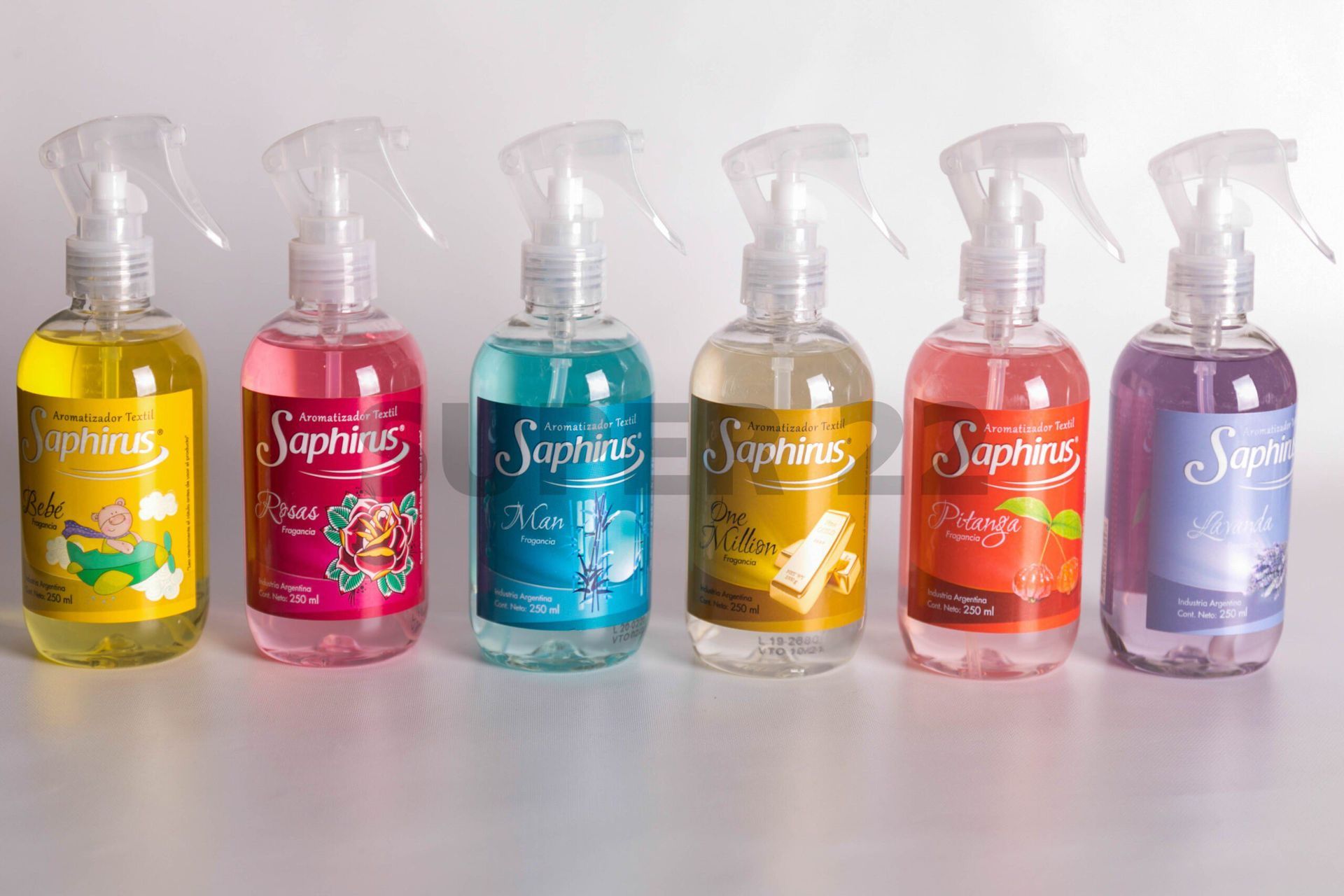 Seis botellas de spray de colores, llenas de producto de limpieza, alineadas sobre una superficie blanca.