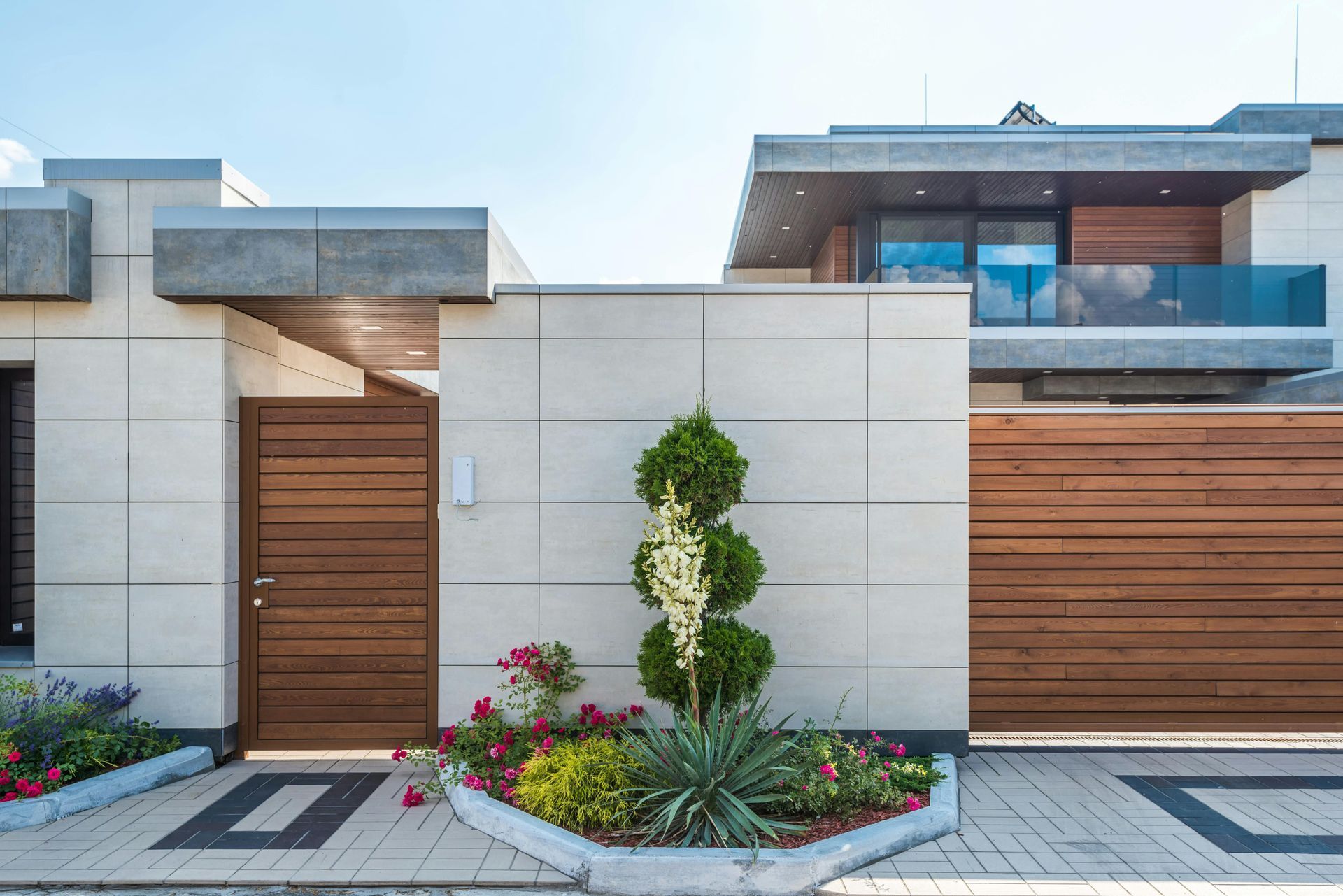 Modern house exterior with wood front door, white walls, and landscaped flower beds