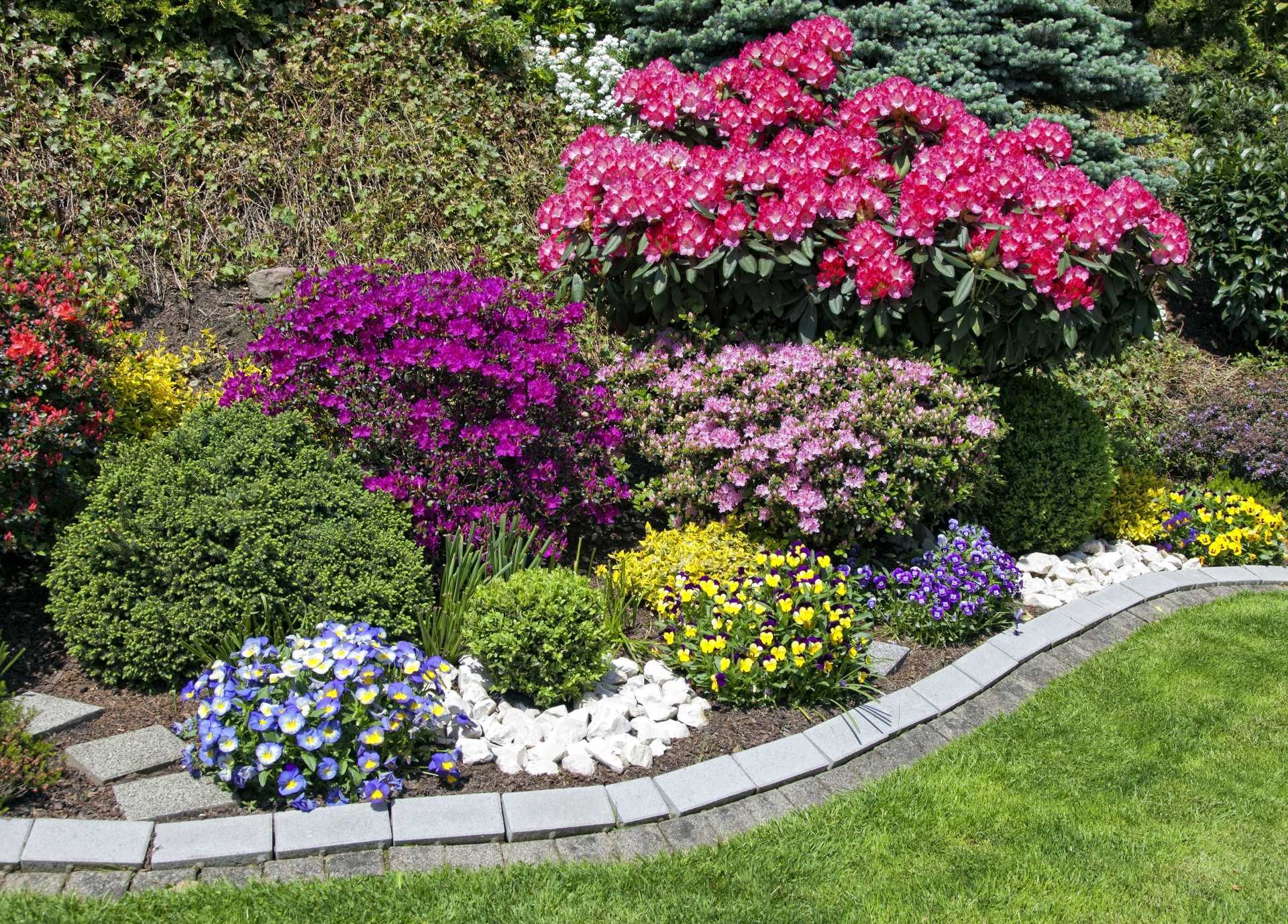 Curved garden border with colorful blooming flowers and shrubs along a stone path