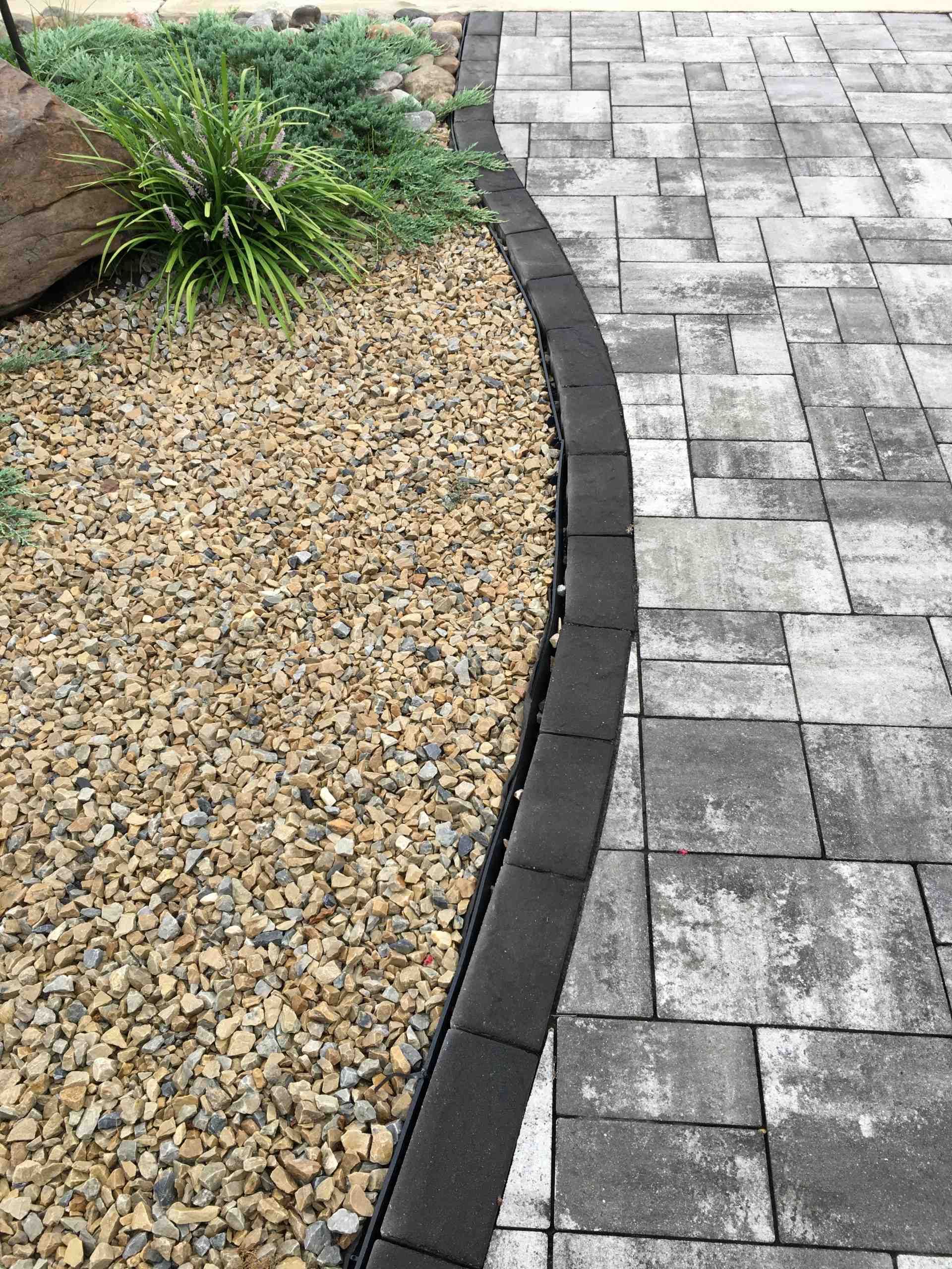 Curved garden border of gravel beside gray paver walkway and low plants