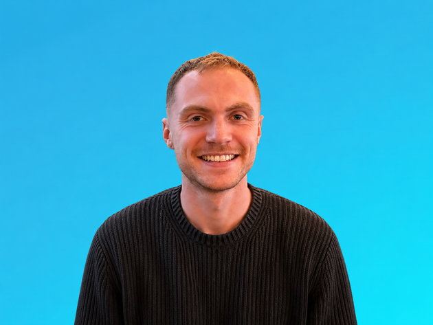 Smiling person in a black sweater against a bright blue background