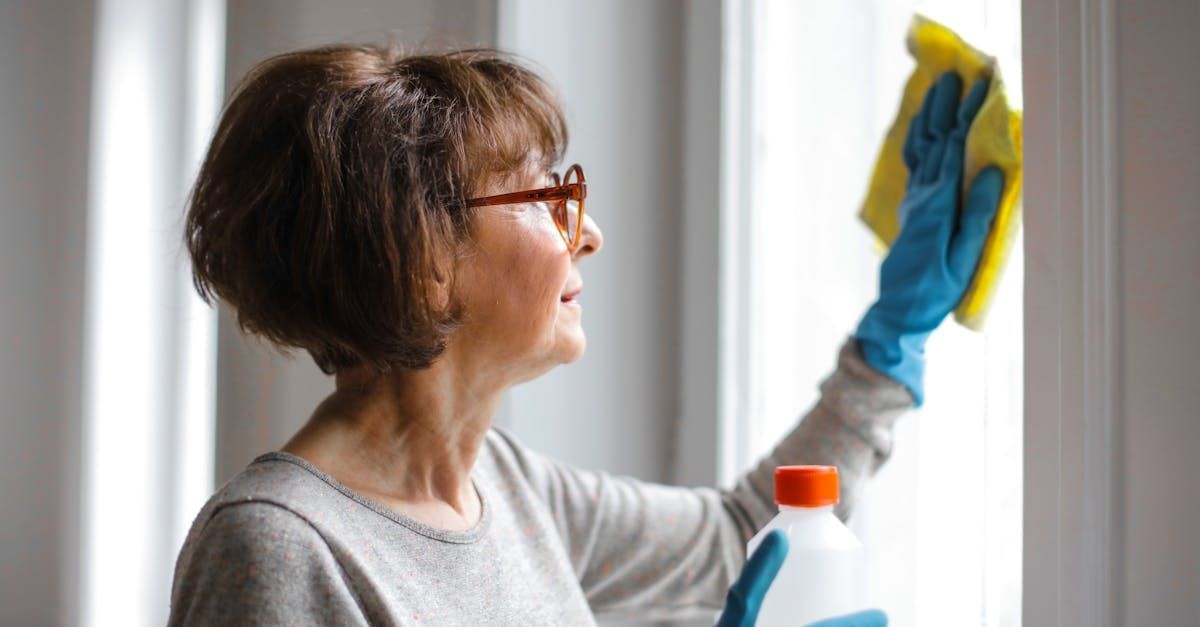 A woman is cleaning a window with a sponge and a bottle of cleaner.