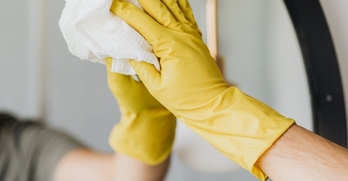 A person wearing yellow gloves is cleaning a mirror with a cloth.