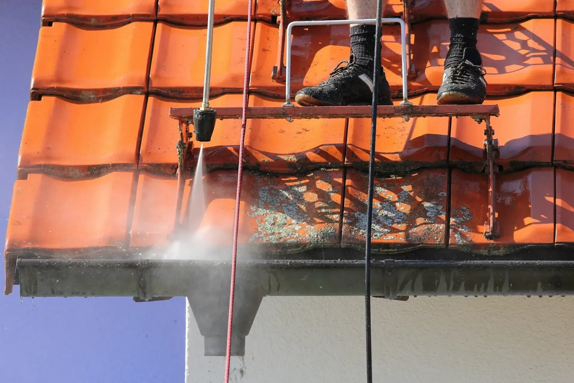 A man is cleaning the roof of a house with a high pressure washer.