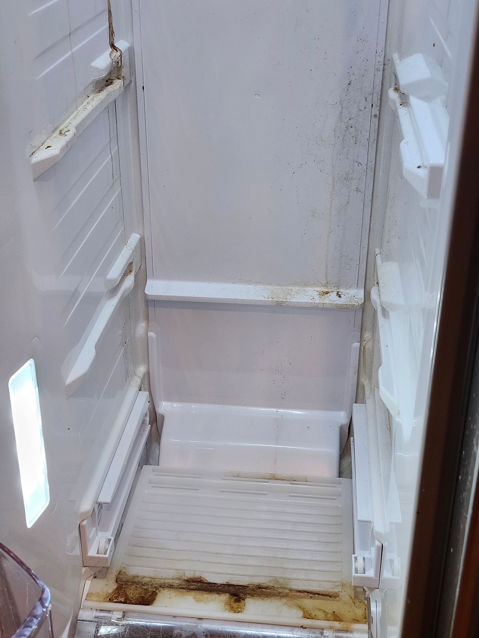 Dirty white shower stall with a stained floor and a built-in seat or ledge