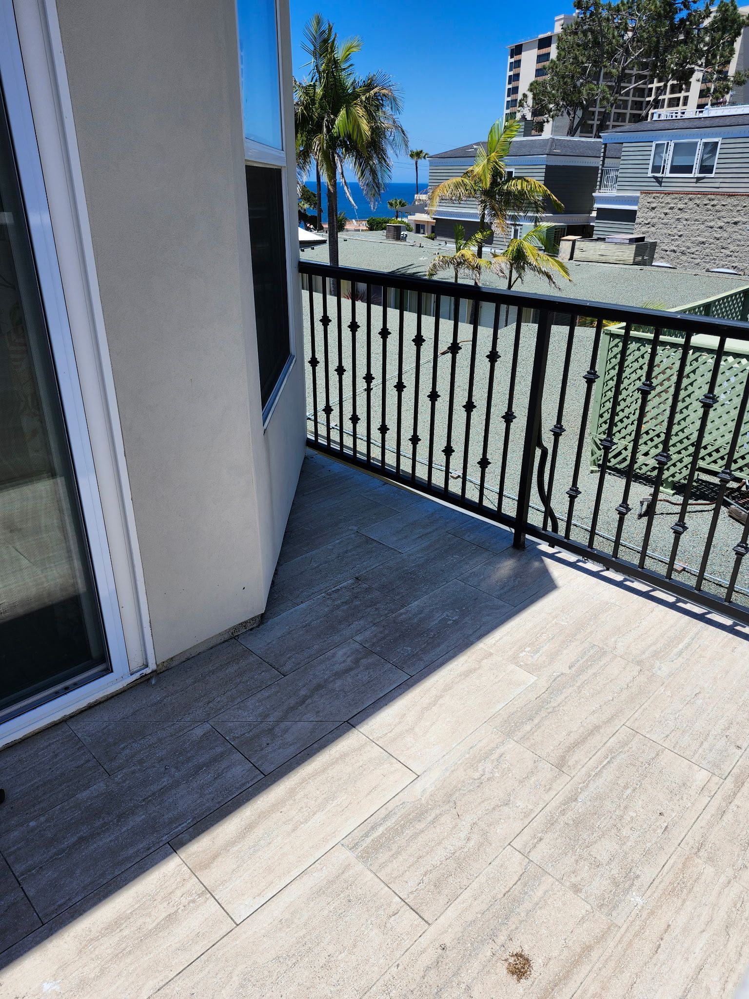 Balcony with light wood floor, black railing, and ocean view under a blue sky