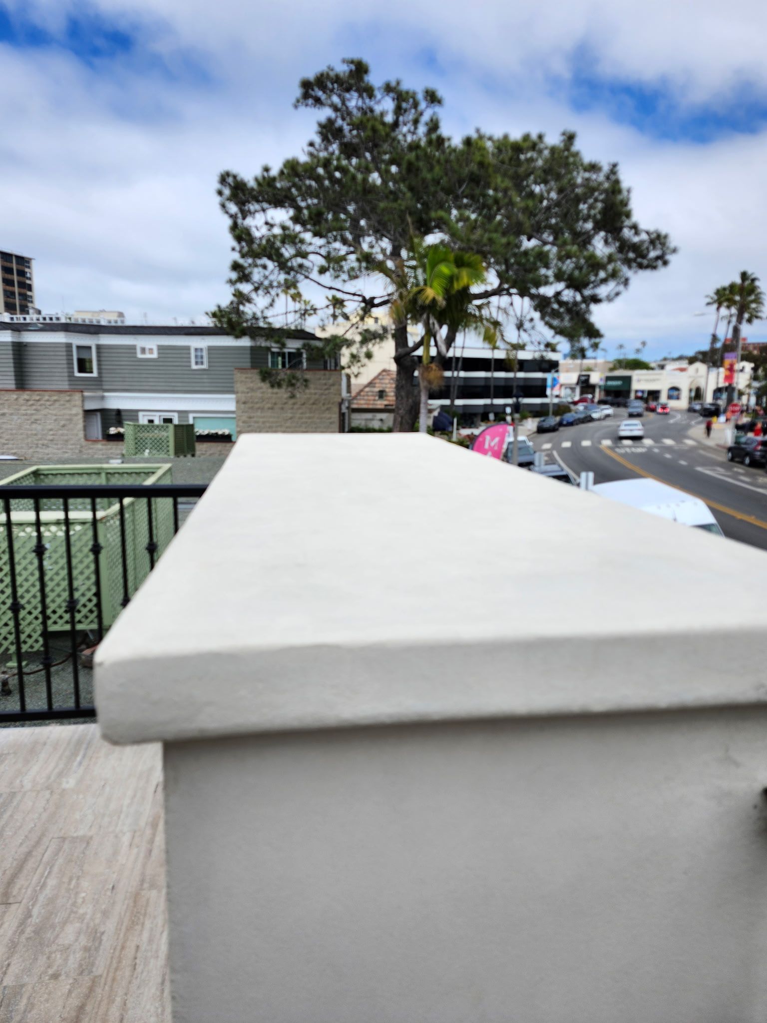 White concrete wall overlooking a street with trees, parked cars, and a cloudy sky