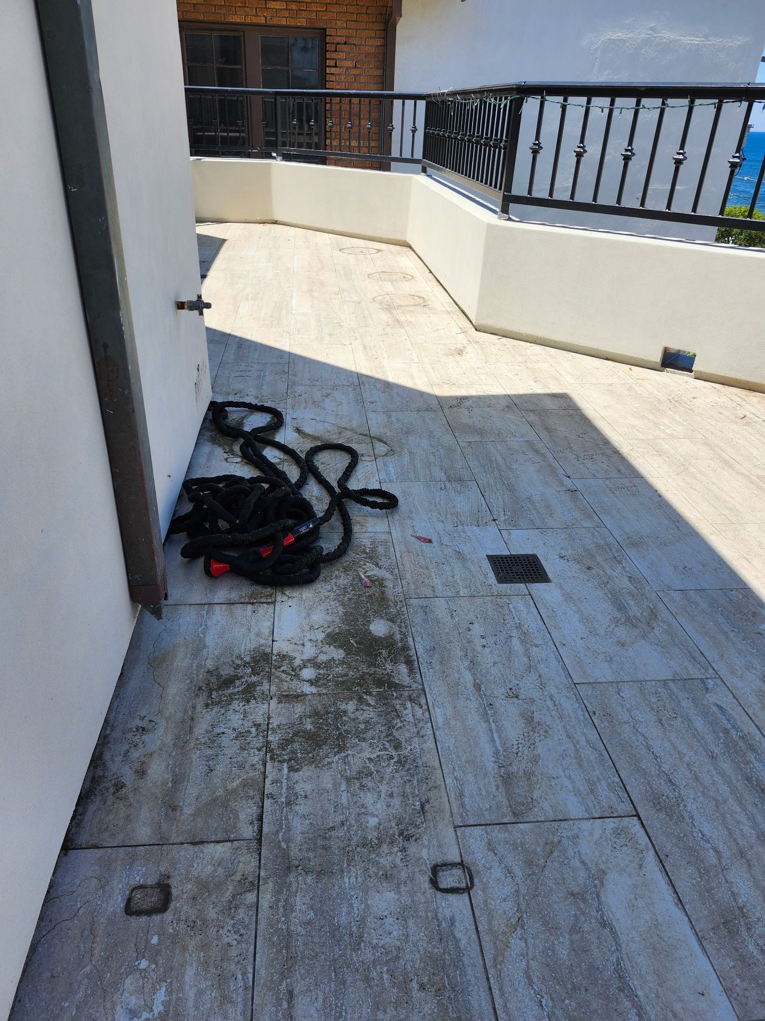 Sunlit balcony walkway with coiled cables on the floor and a black railing overlooking water
