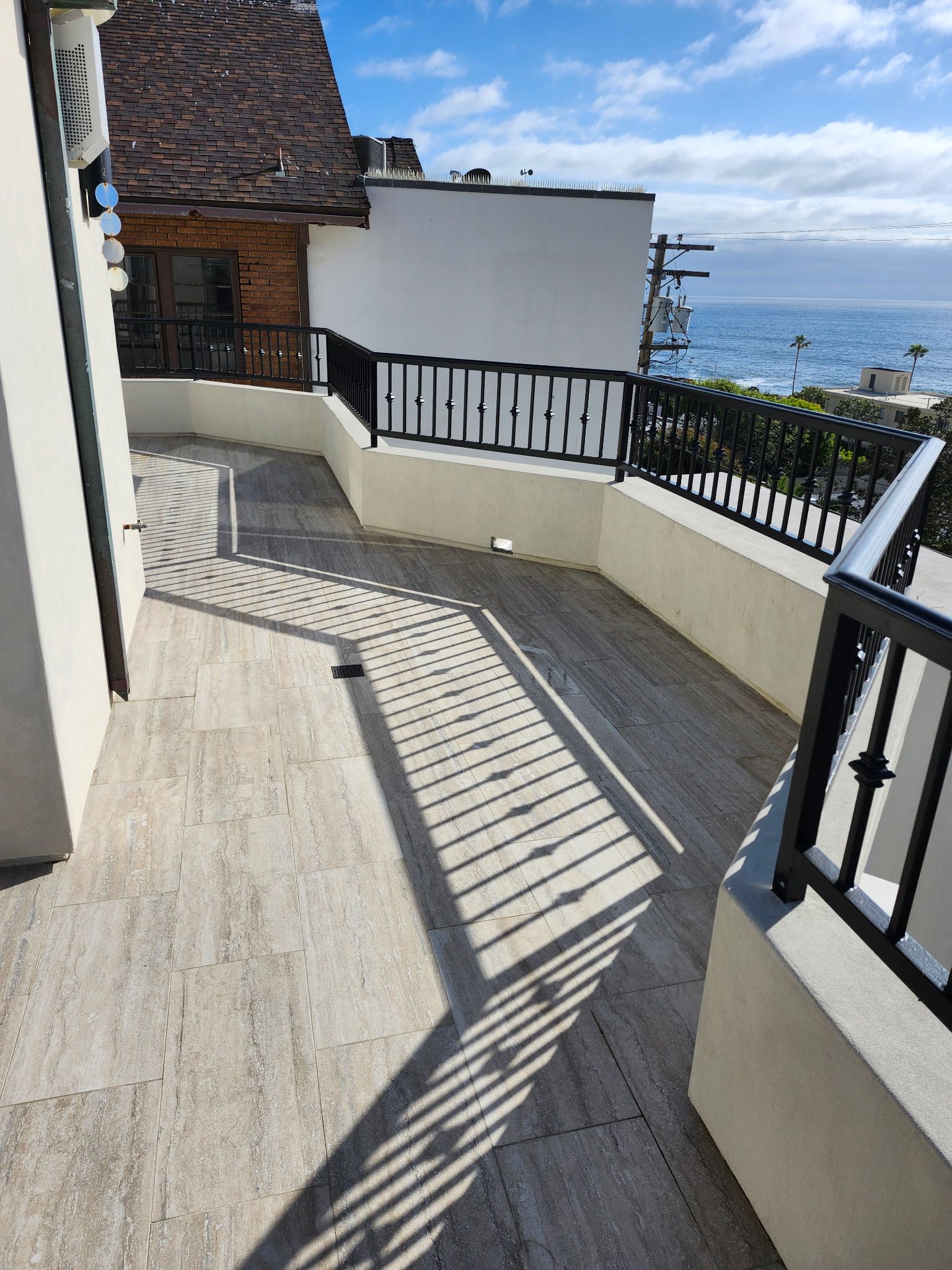 Curved seaside terrace with cream walls, black railings, and ocean view casting striped shadows on the floor