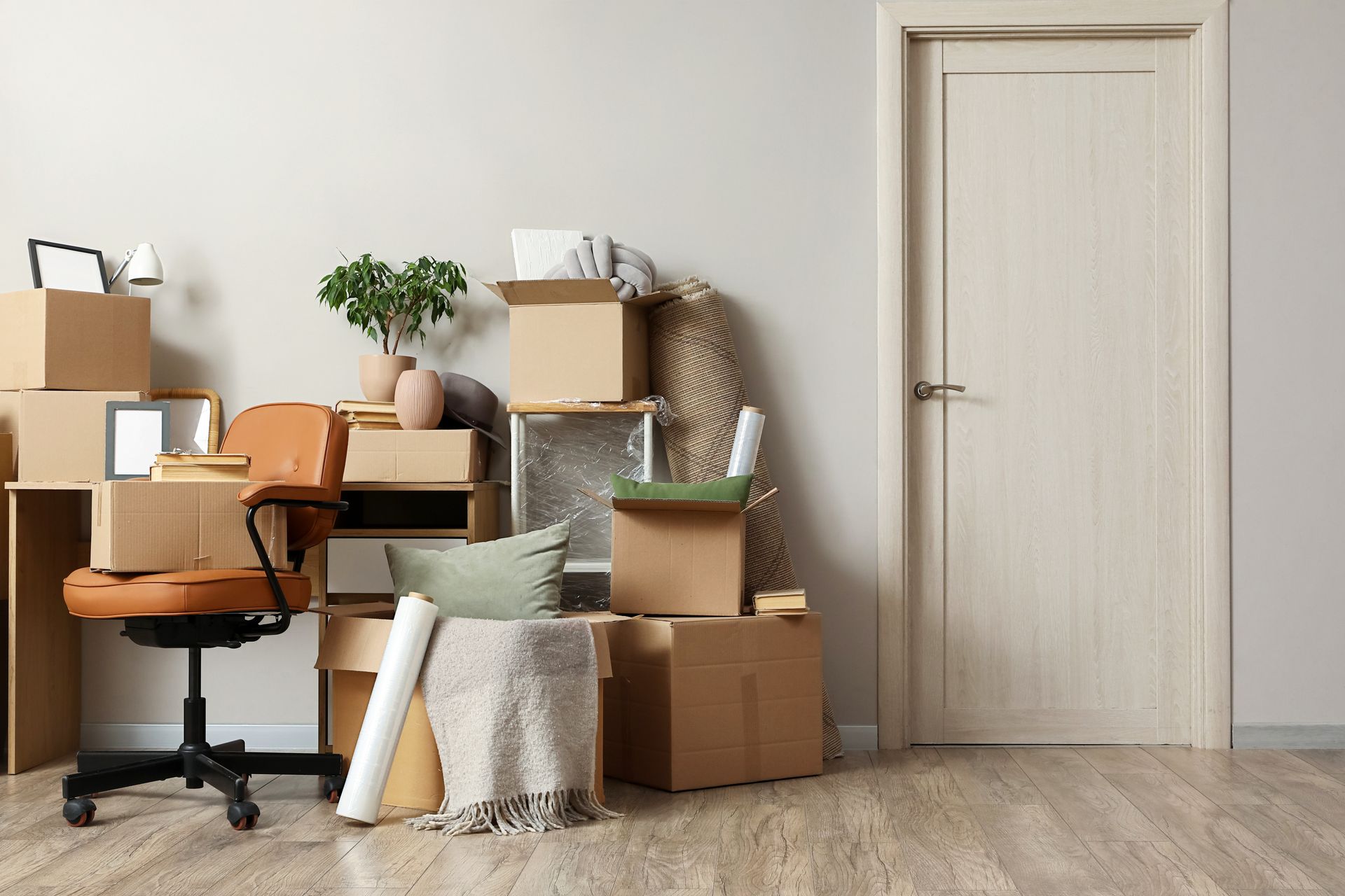 Moving boxes and furniture in a small room beside a closed door, suggesting a recent move or packing up.