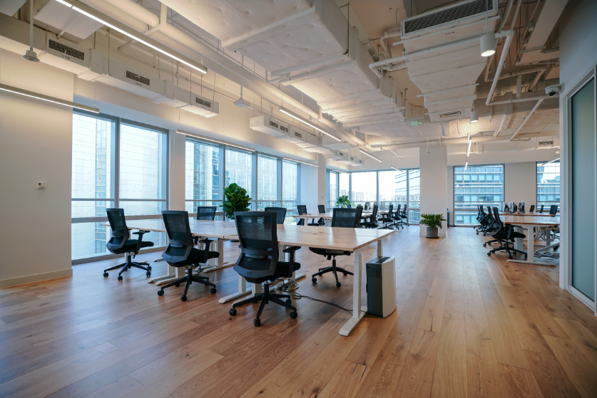 Modern open-plan office with desks, rolling chairs, wood floors, and large windows