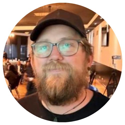 Person with glasses and cap in a warmly lit indoor venue, looking at the camera.