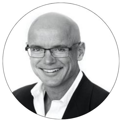 Smiling bald man in glasses wearing a dark blazer and white shirt on a white background