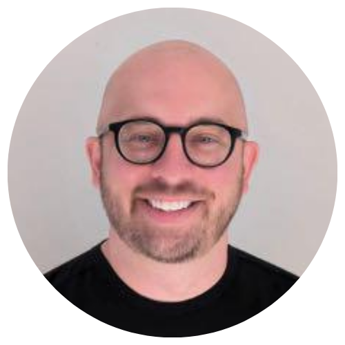 Smiling bald man with black glasses and beard on a light gray background